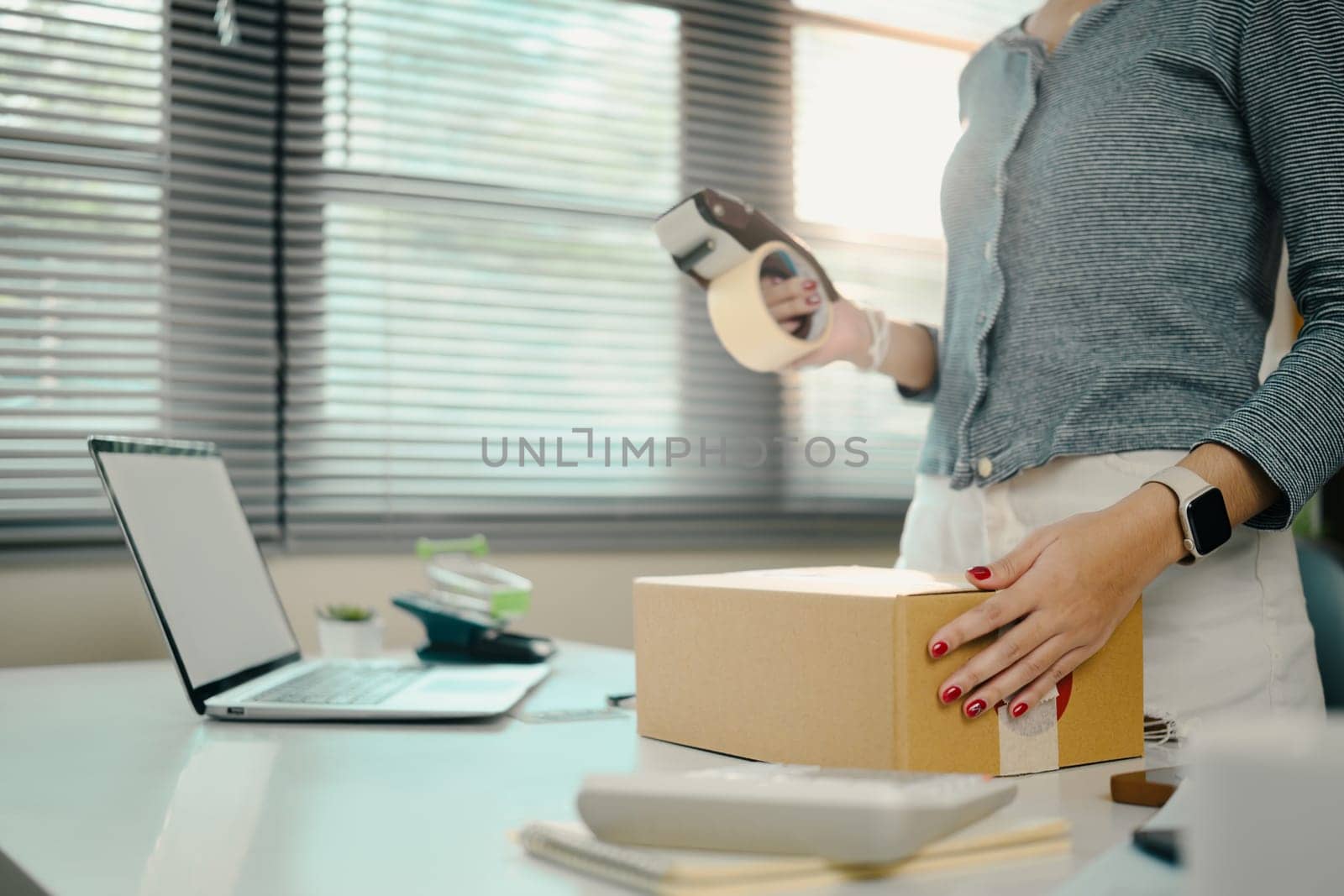 Young small business owner packing products for shipping in her home office.
