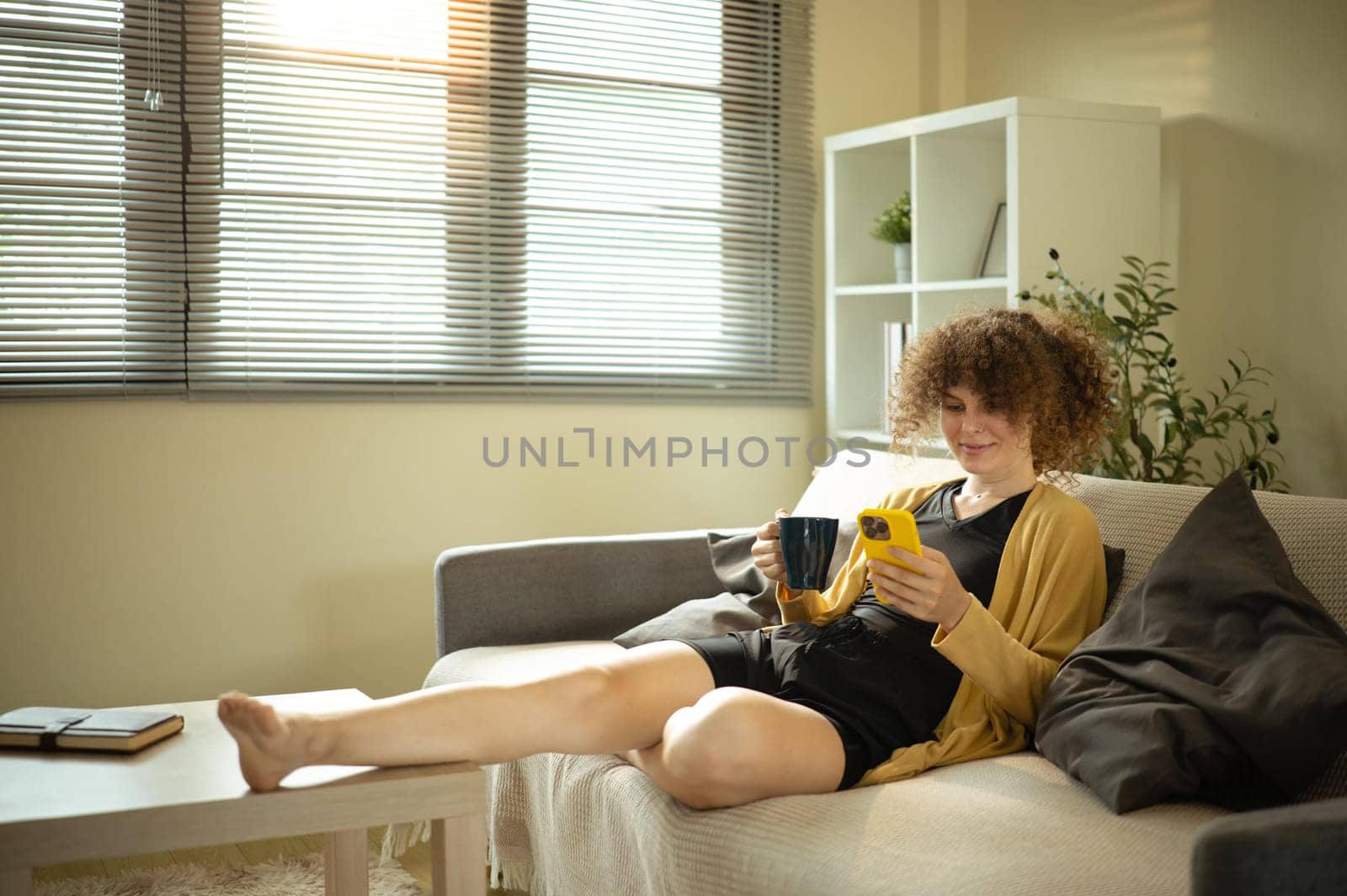 Young woman with curly hair lounging on the sofa and using her smartphone.