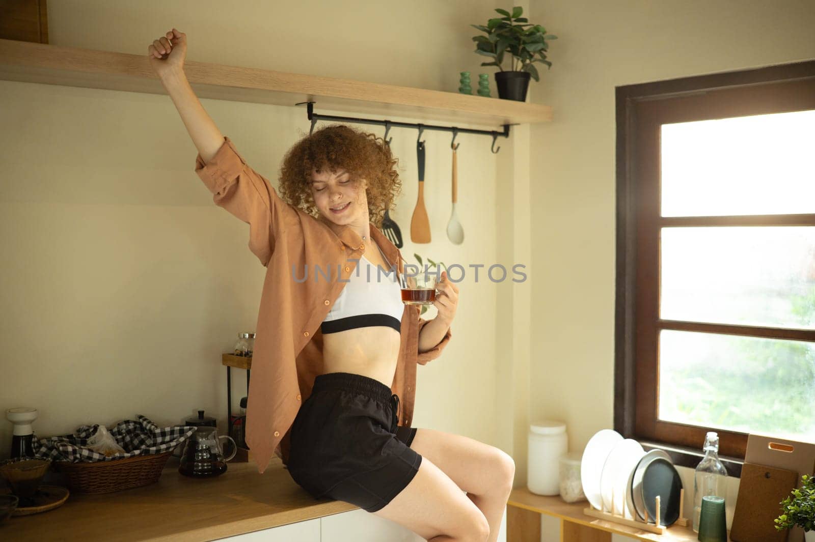 Home lifestyle scene of woman with curly hair enjoying a warm drink in her kitchen.