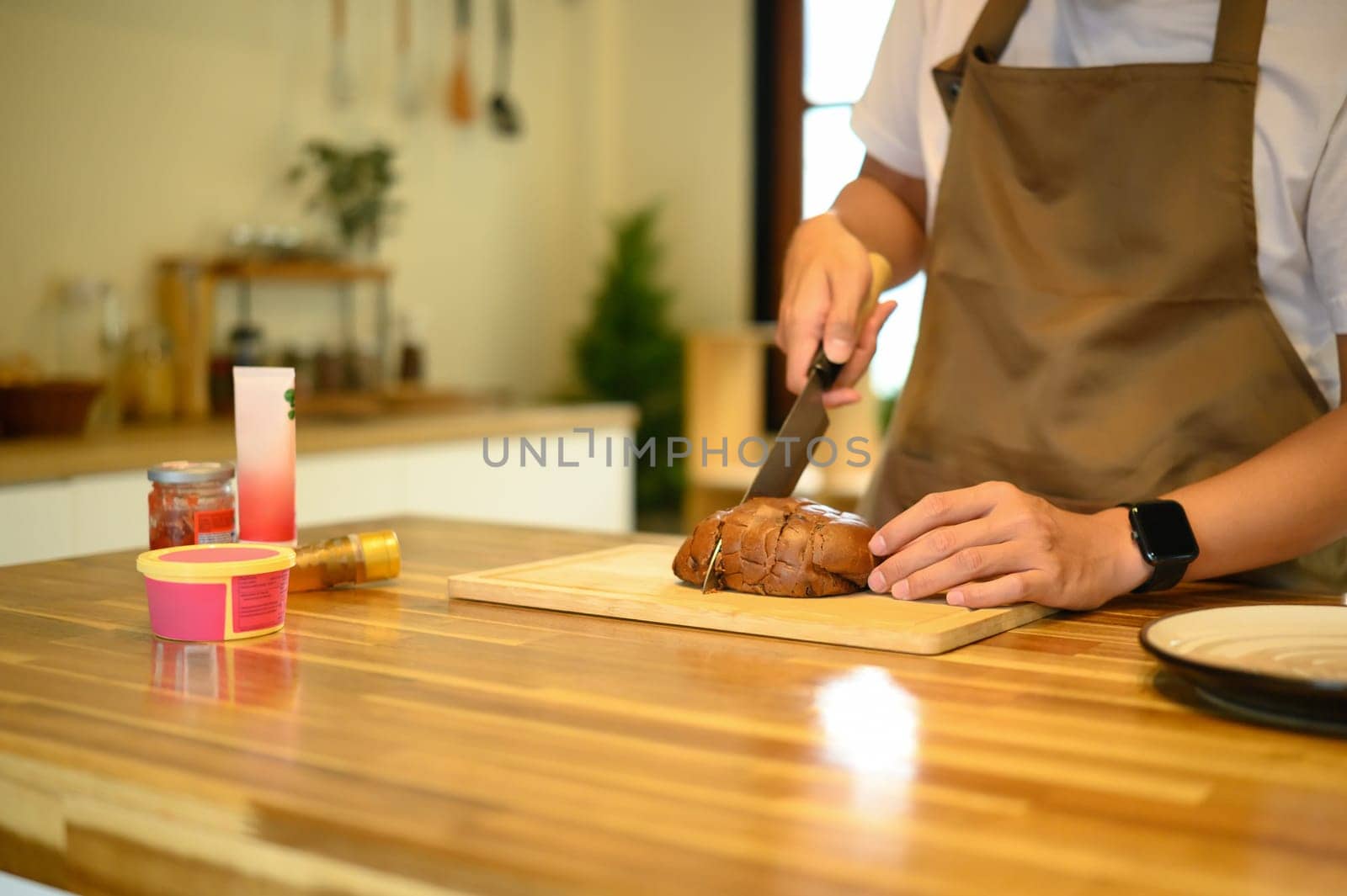 Man preparing breakfast by slicing loaf of bread, with ingredients arranged on a wooden countertop.
