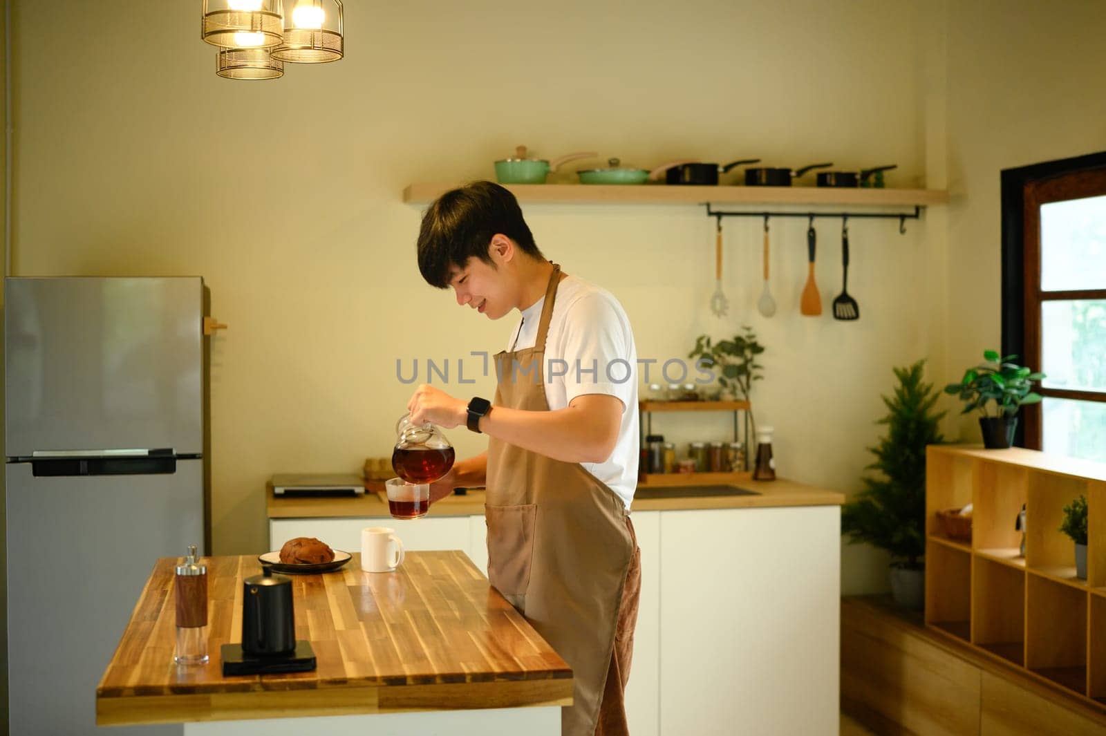 Man pouring freshly brewed coffee into a mug in a kitchen with warm lighting.