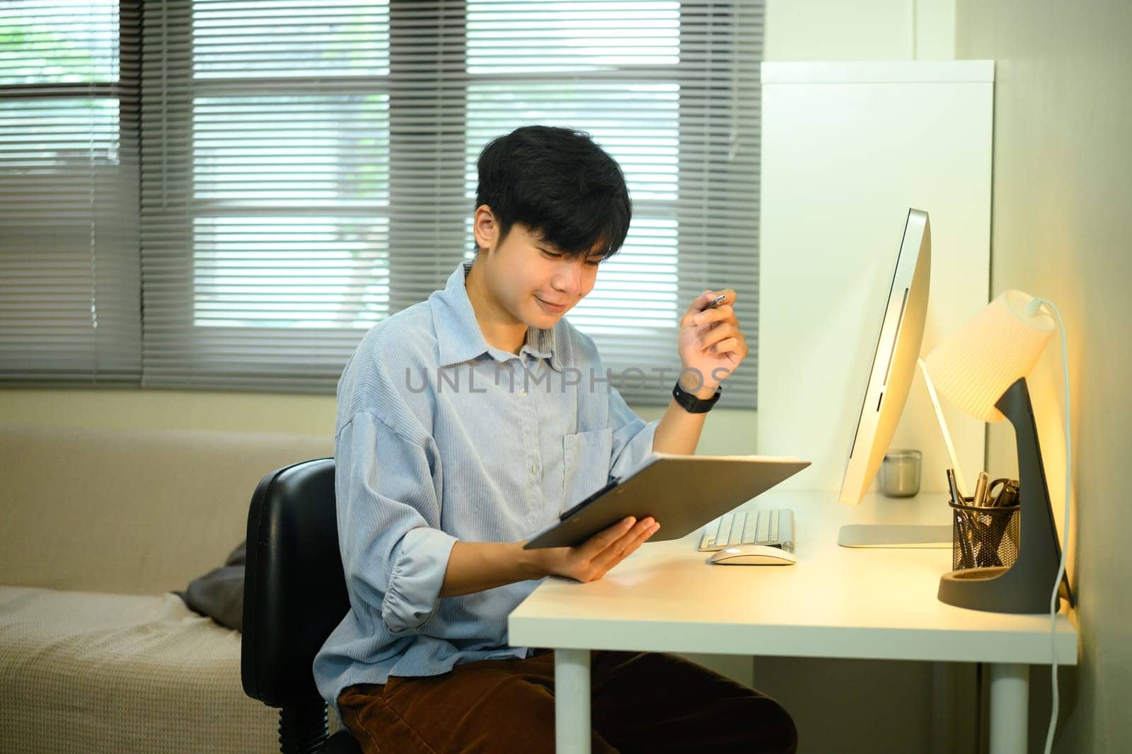Smiling asian entrepreneur working from home and reviewing documents at a desk.