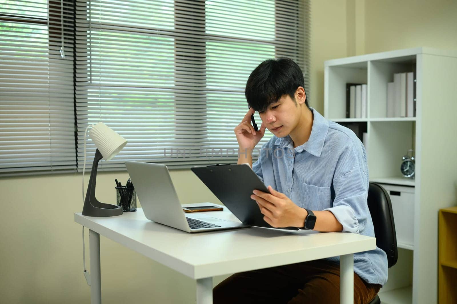 Focused freelancer reviewing documents at modern white desk with digital devices.