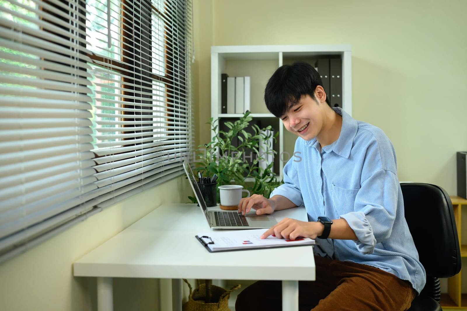 Smiling asian entrepreneur using a digital tablet while working from home at a modern desk.