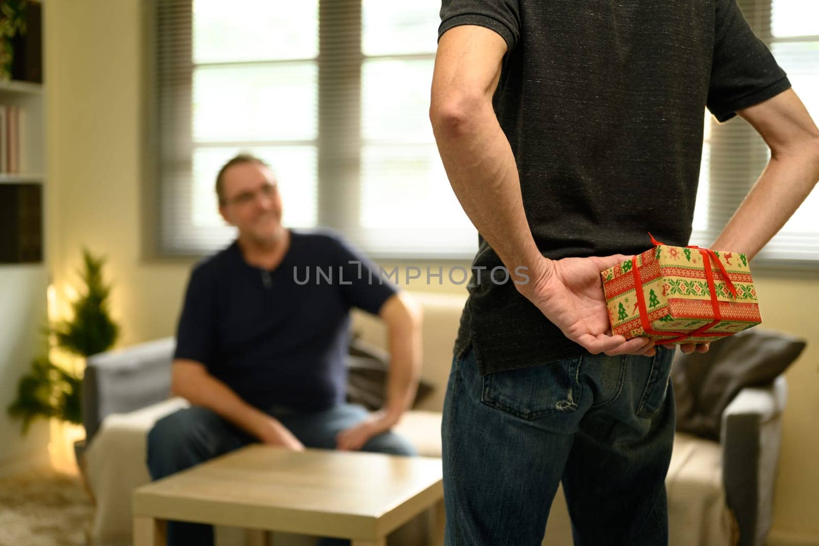 Adult son preparing surprise gift for his father, hiding a present behind his back. Fathers day concept.