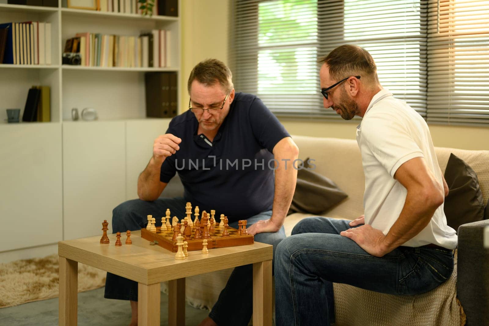 Father and adult son enjoying a game of chess in cozy living room. Fathers day concept..