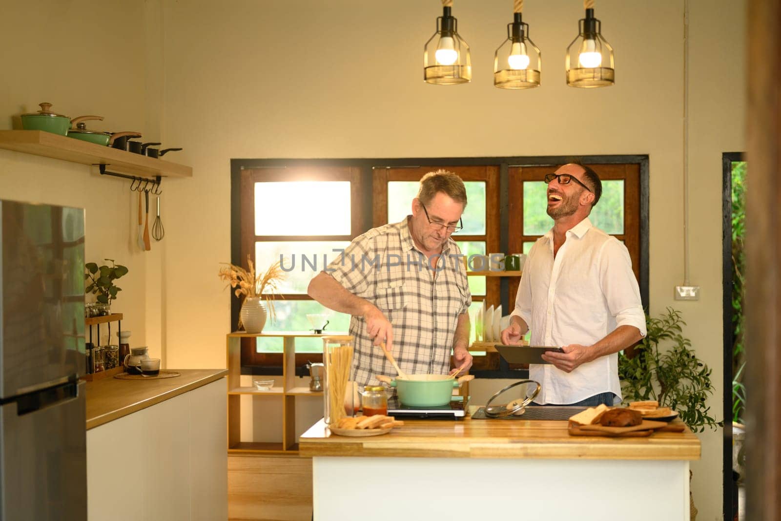 Father and adult son sharing laughter while cooking in a cozy home kitchen. Fathers day concept.