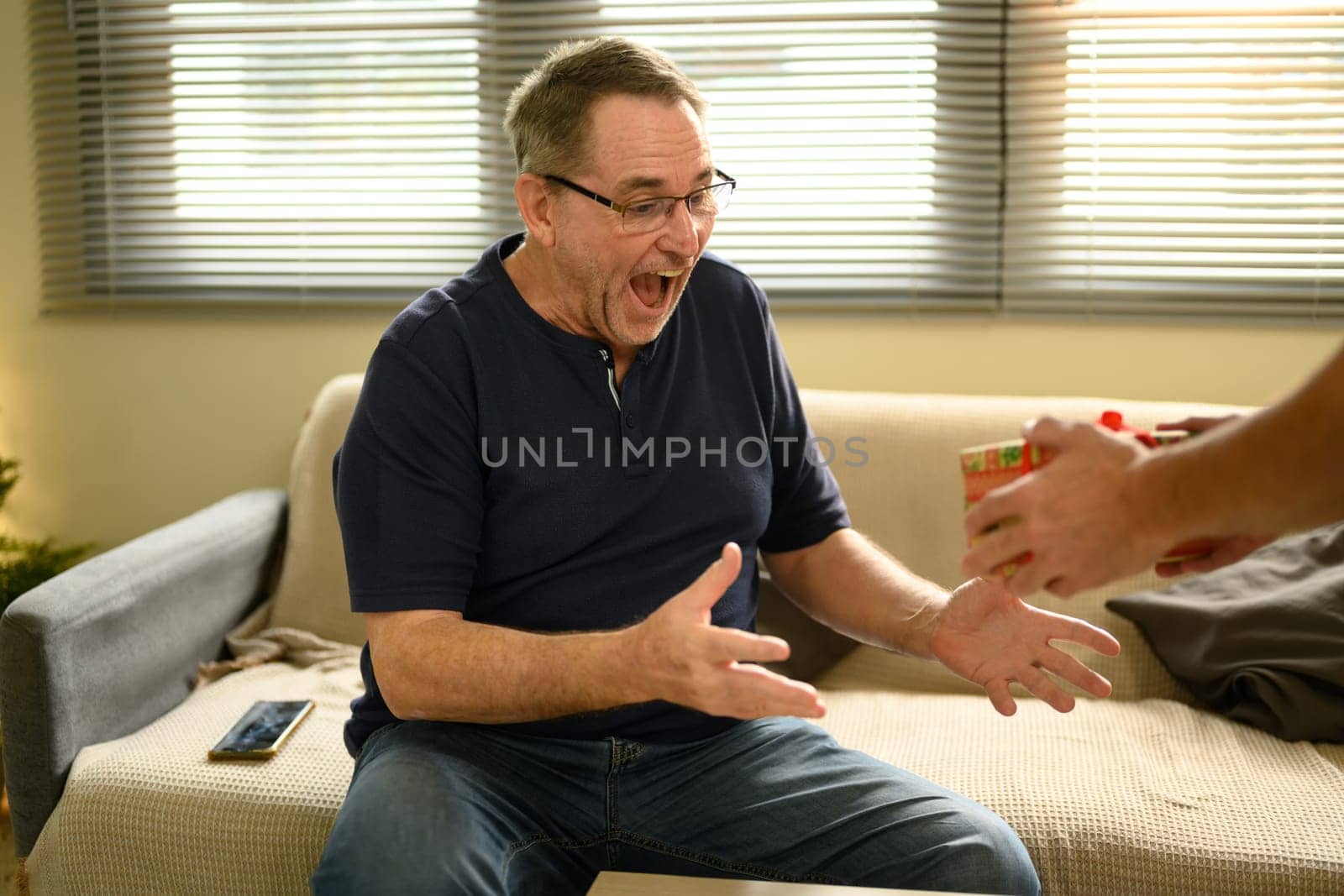 Excited father reacts with joy as his son presents him with a surprise gift. Fathers day concept.