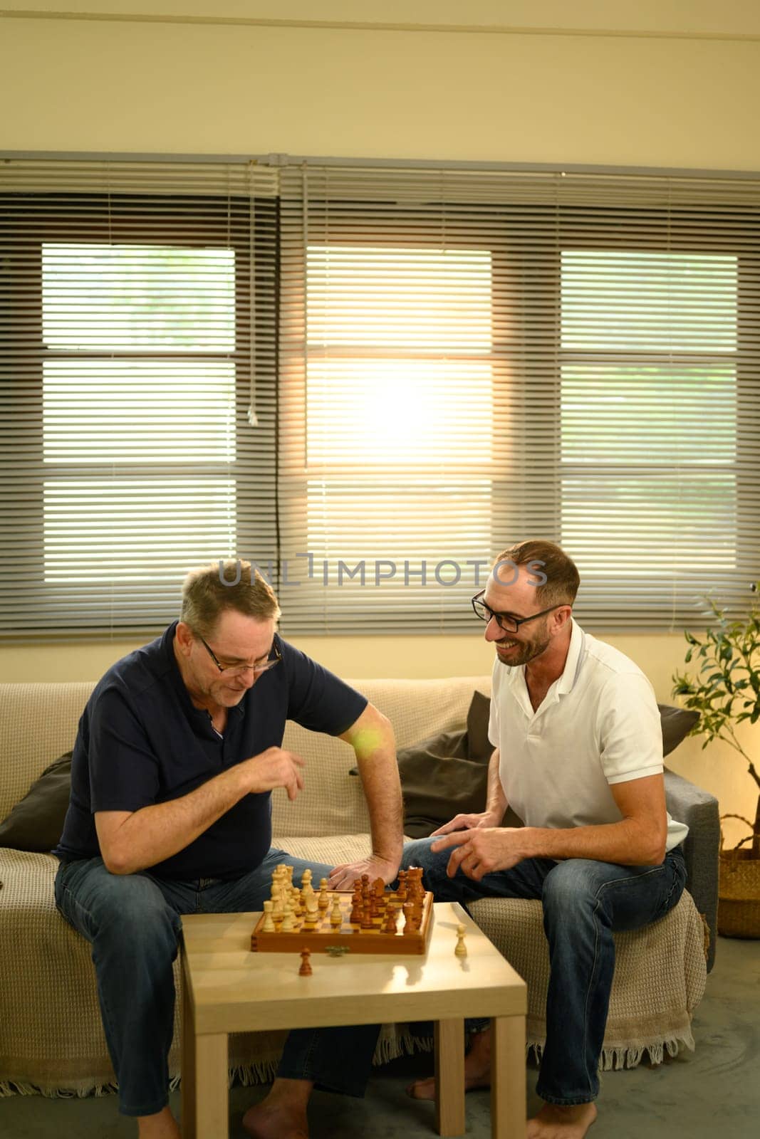 Father and adult son enjoying a game of chess in cozy living room. Fathers day concept..