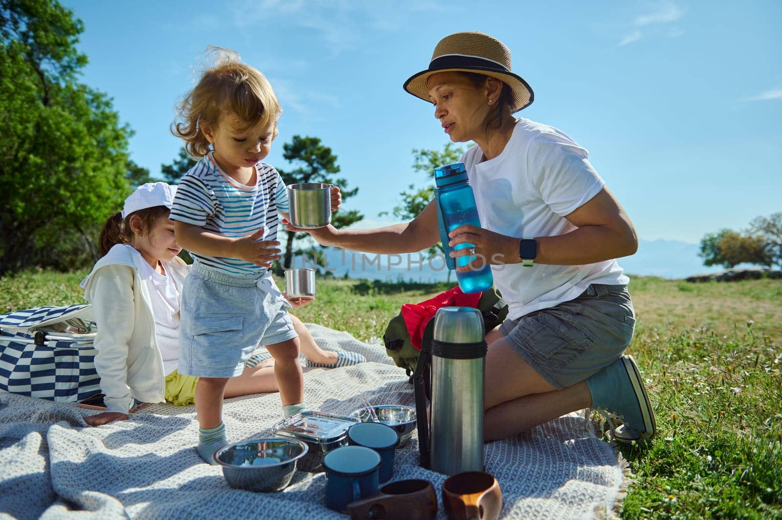 A mother and her children enjoy a sunny picnic amidst scenic nature, celebrating outdoor bonding and family relationships in a serene mountain setting.