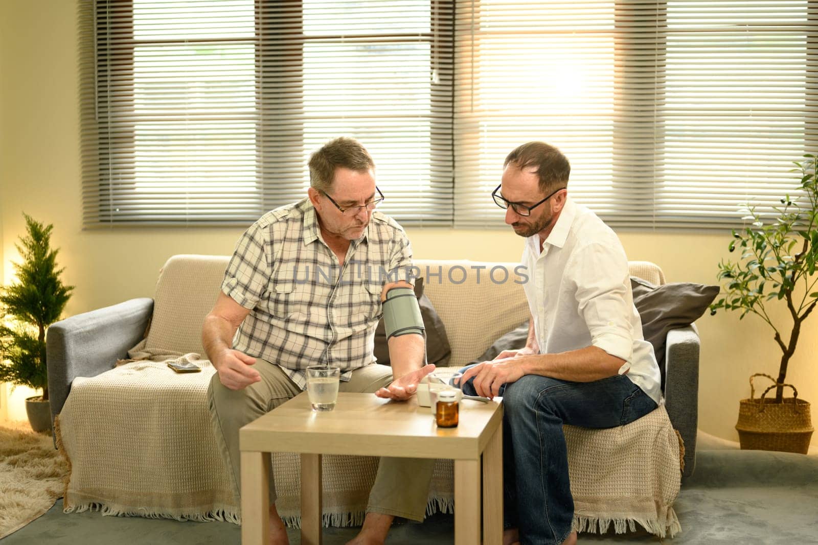 Adult son checking elderly father blood pressure at home. Fathers day concept.