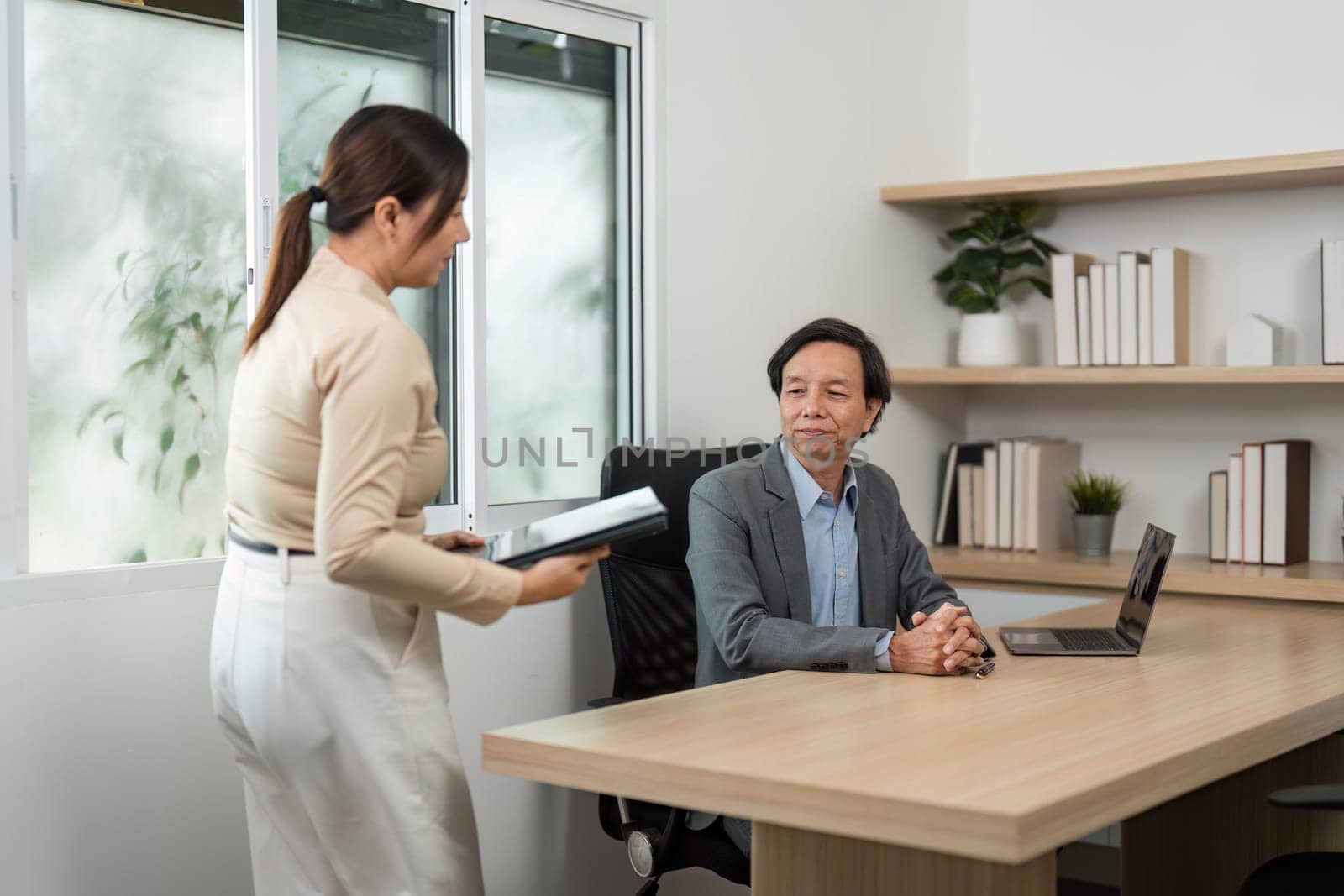 A businesswoman hands over documents to a businessman during a meeting, showcasing teamwork and professional collaboration in a modern workspace.