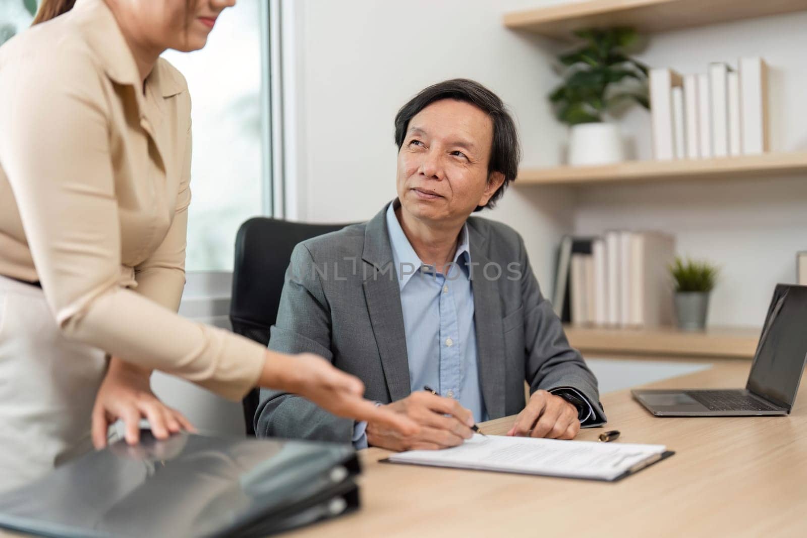 A businessman reviews and signs documents while discussing with a colleague, emphasizing collaboration and attention to detail.