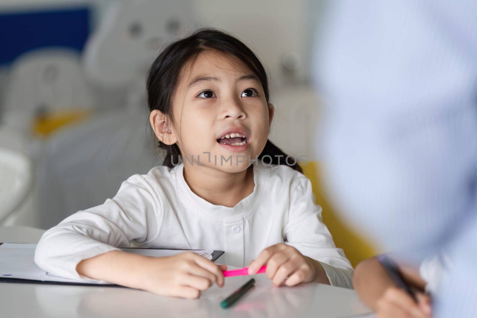 A curious young girl listens attentively in class, showcasing engagement and enthusiasm for learning in a vibrant educational environment.