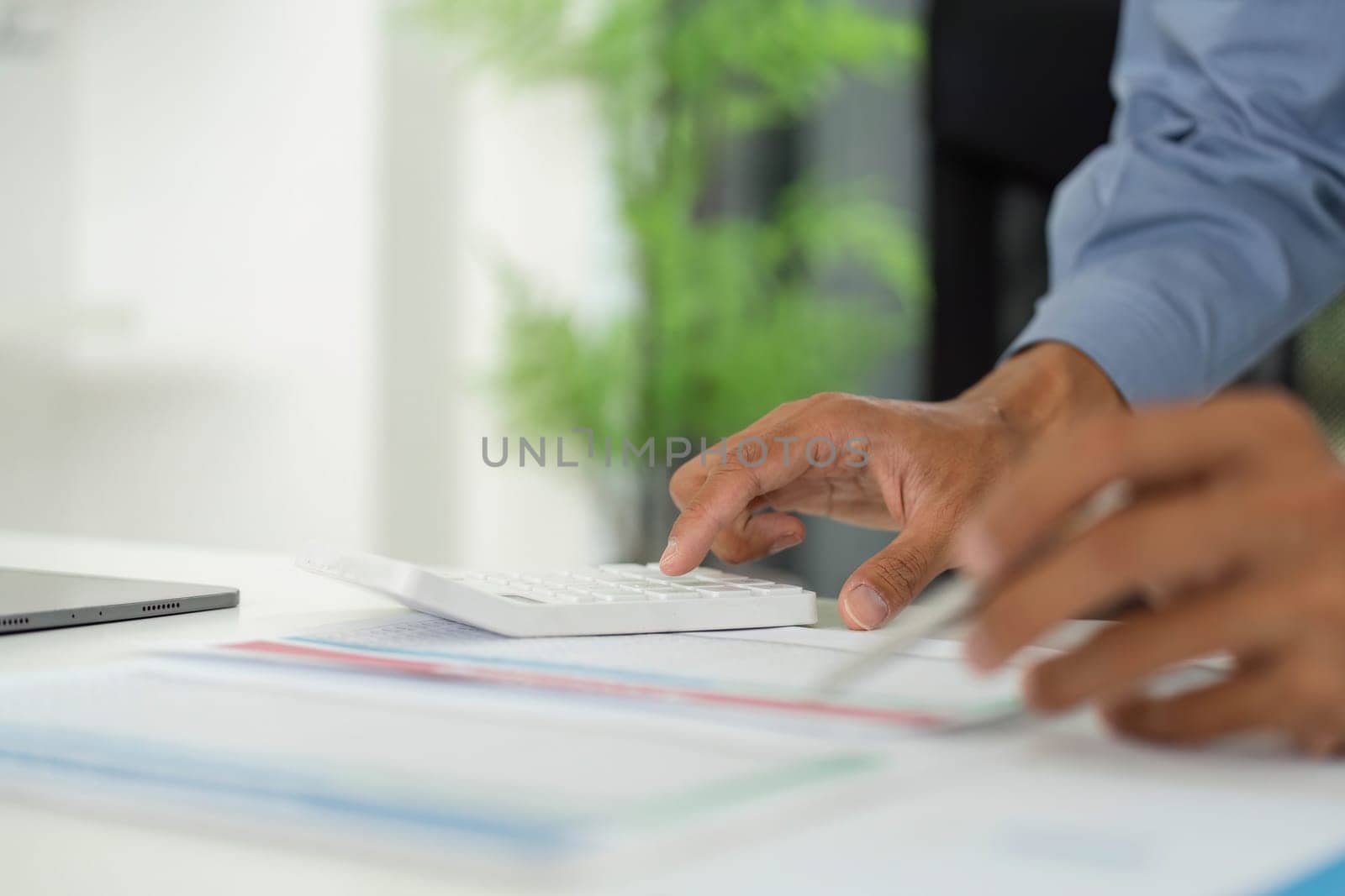 A professional's hand operates a calculator, analyzing reports and data on a modern office desk.