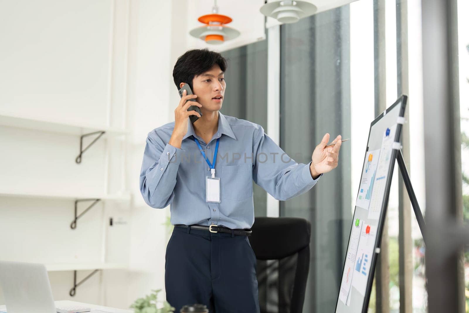 A young businessman discusses strategic insights from a whiteboard while speaking on the phone in an office environment.