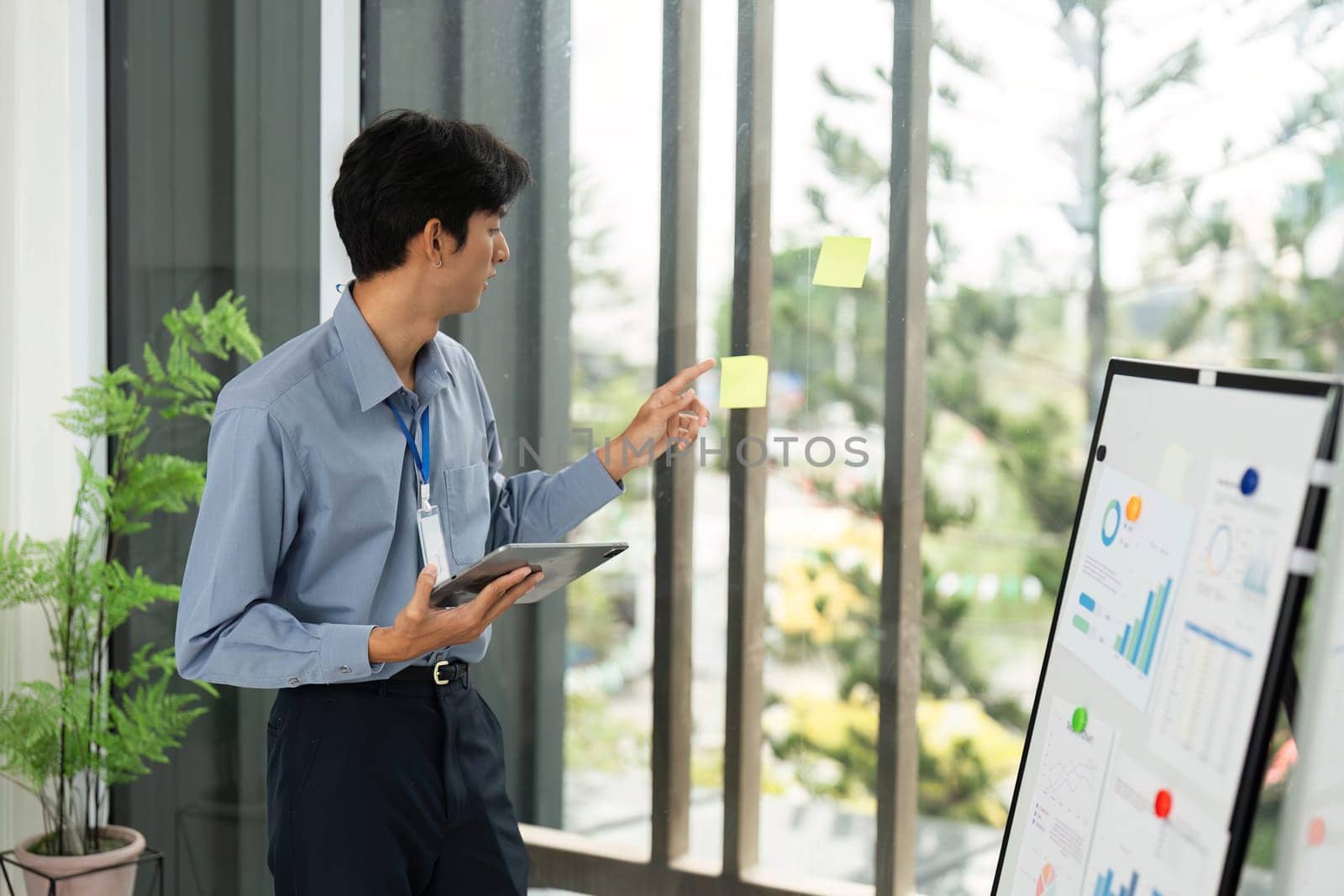 A focused businessman presenting ideas during a remote work strategy session, utilizing a digital tablet and sticky notes for brainstorming.
