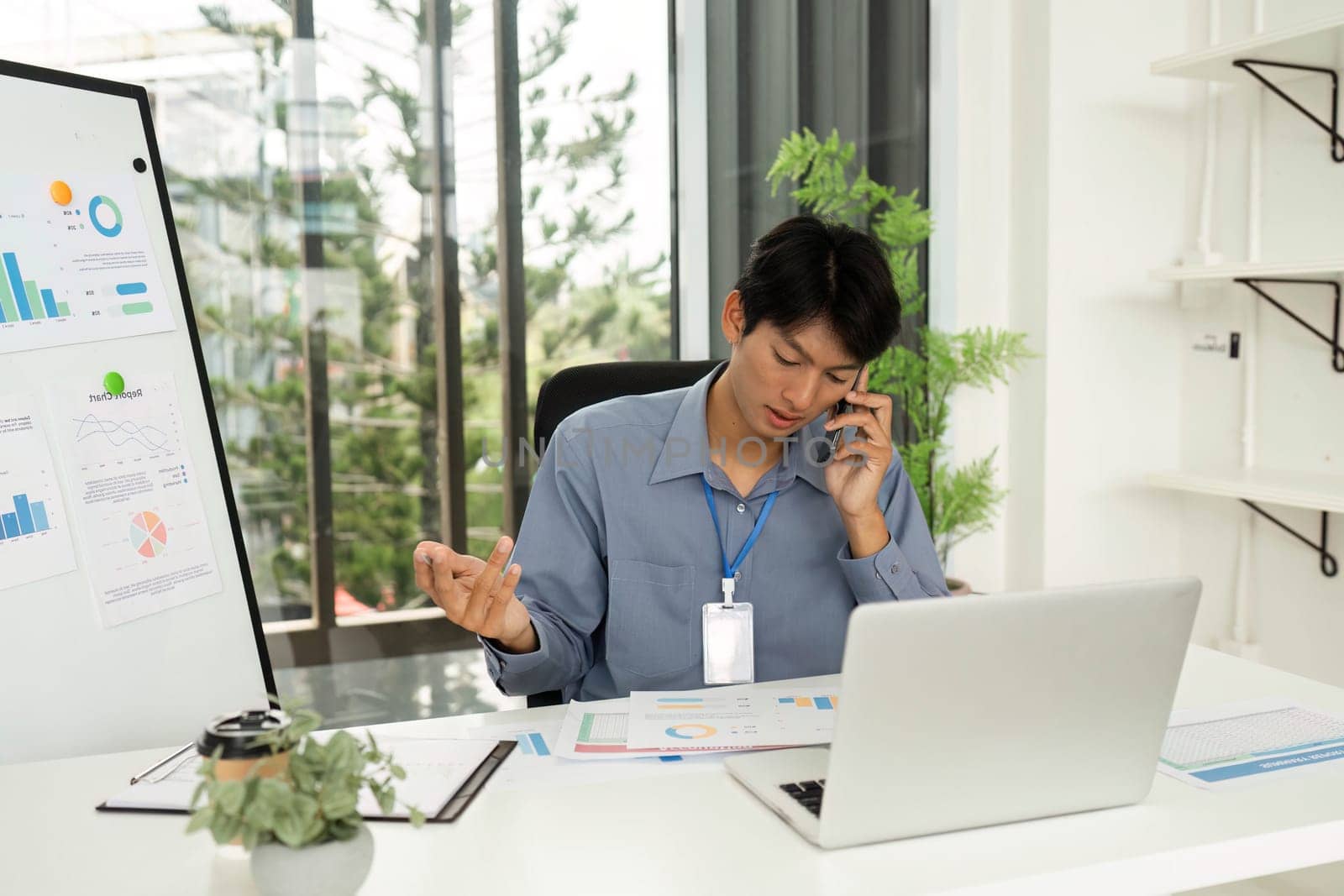 A young man reviewing financial charts and discussing insights over the phone in a bright, modern office space.