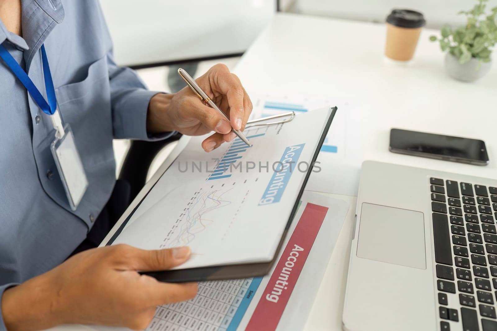 An accountant reviewing financial graphs and data on a clipboard while working on a laptop, showcasing focus on financial analysis.
