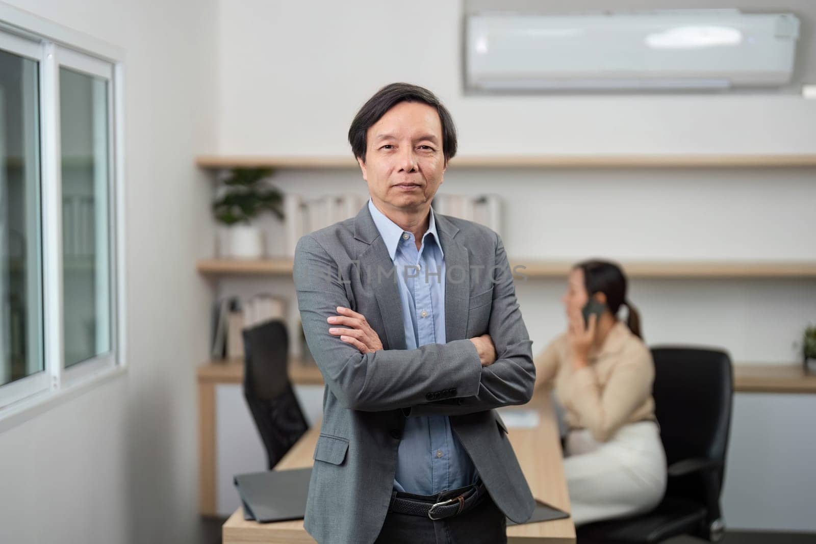 A confident businessman poses in a modern office, demonstrating leadership qualities while a colleague works in the background.