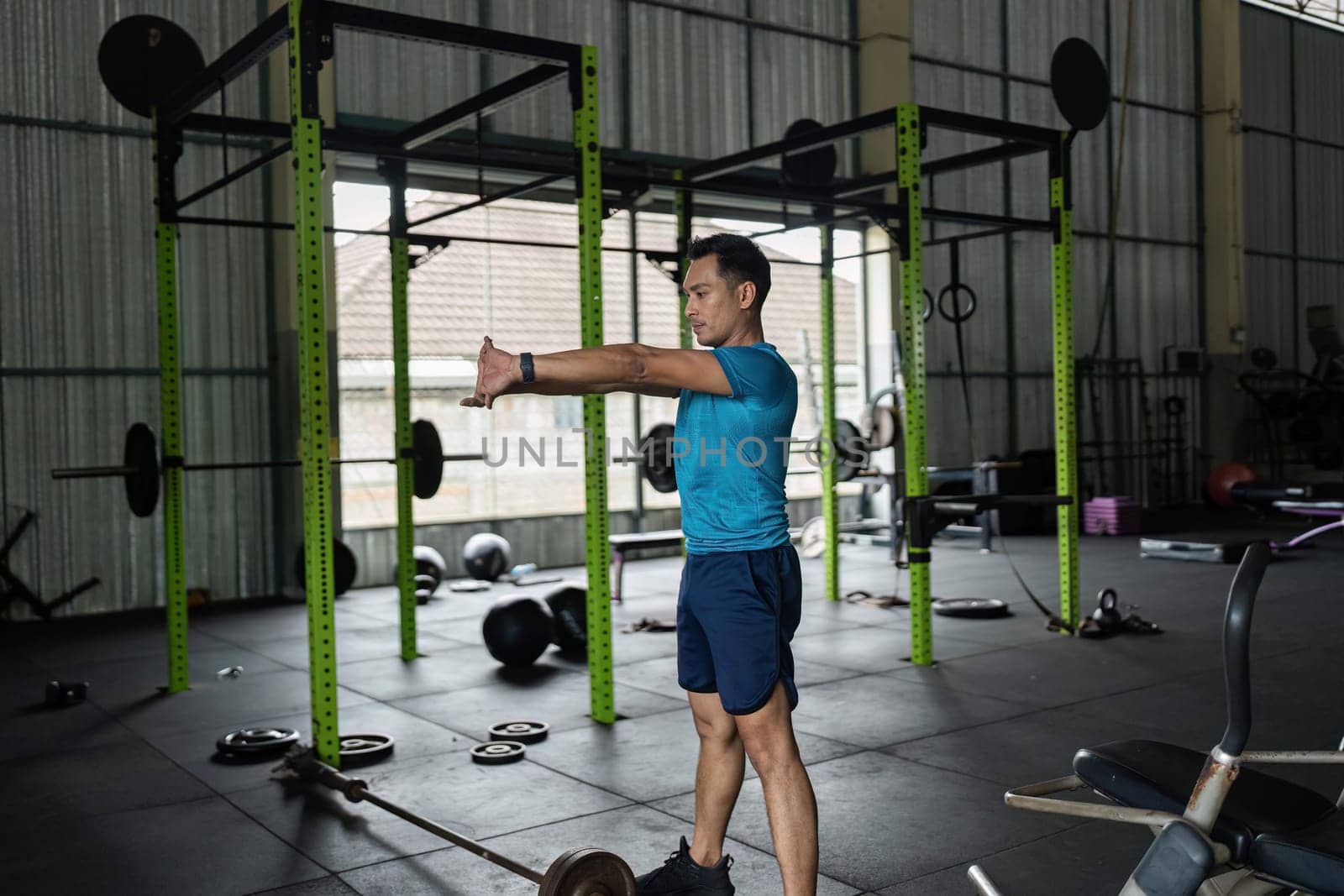 A fit male prepares for his workout by stretching his arms in a gym, emphasizing the importance of warm-up.