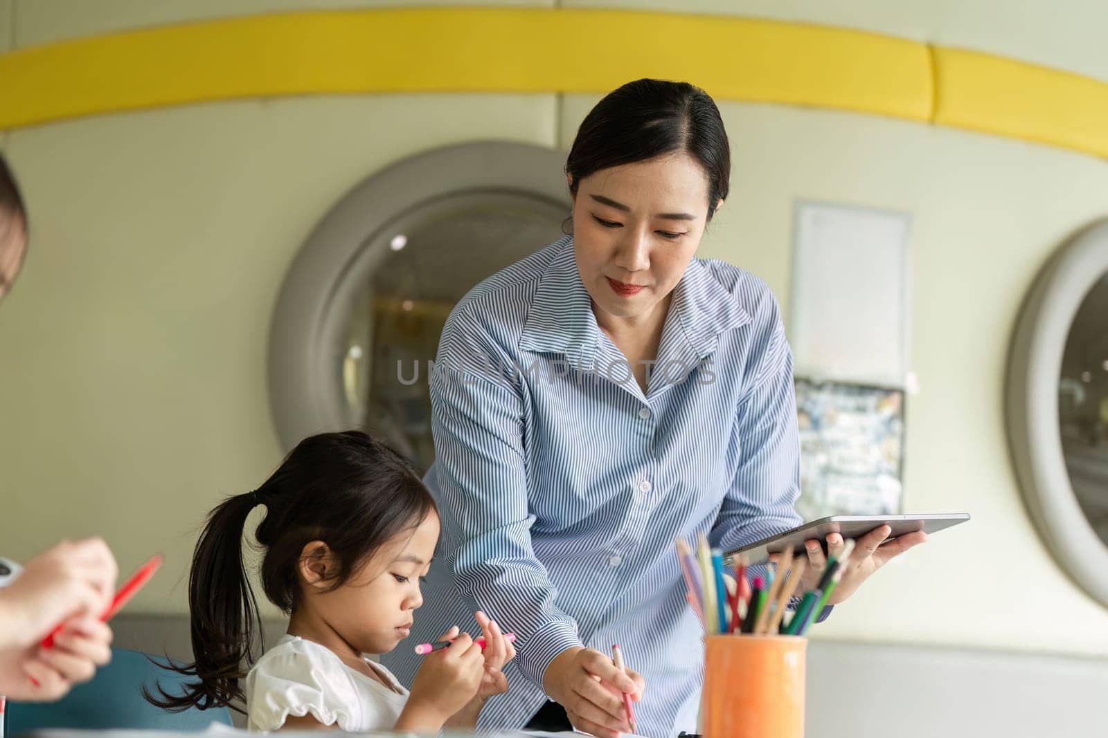 A teacher provides support to a young girl as she works on her art project, fostering creativity in a vibrant classroom setting.
