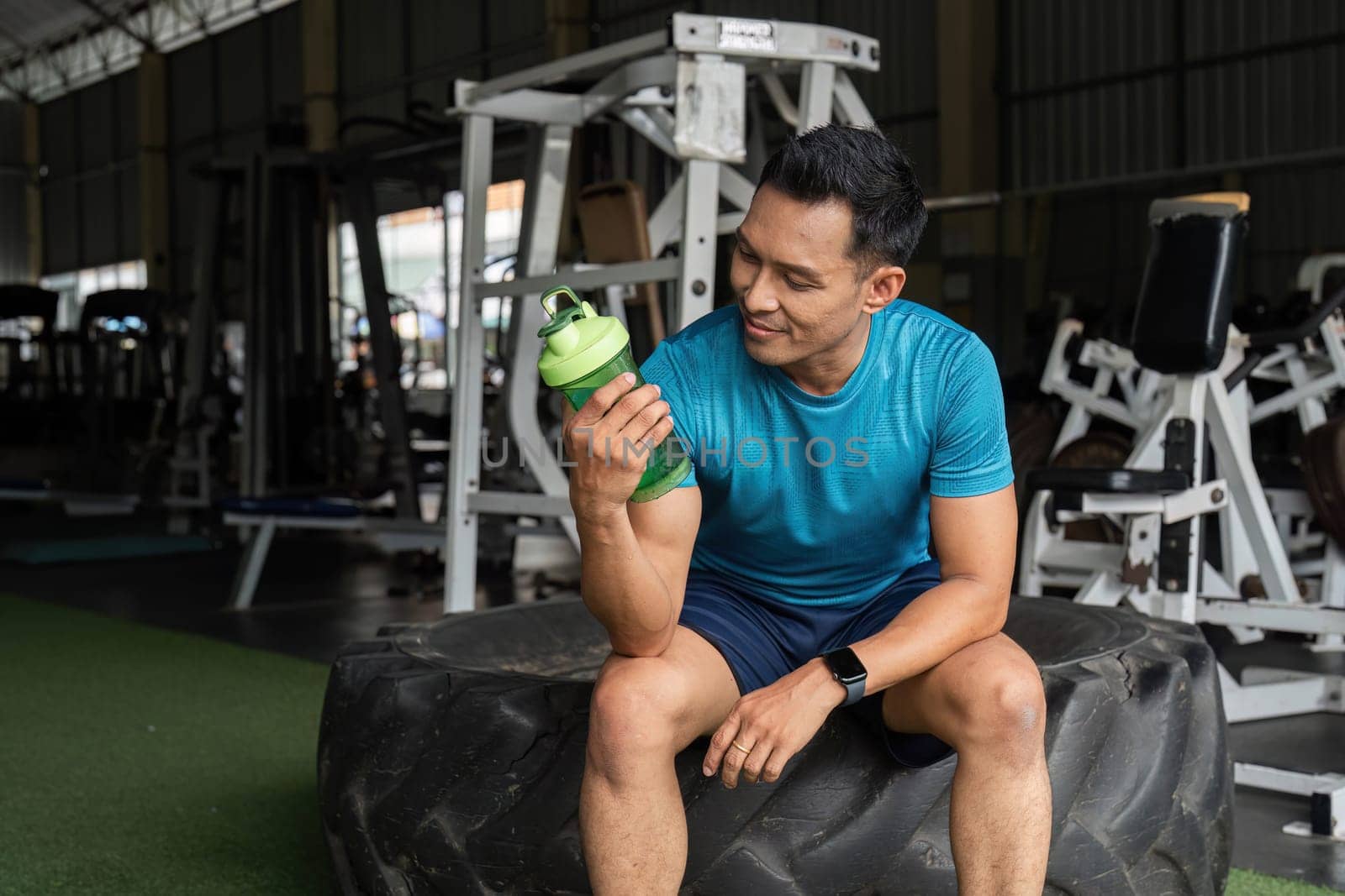 A fitness enthusiast inspects his protein shaker, reflecting on hydration and nutrition in a gym environment.