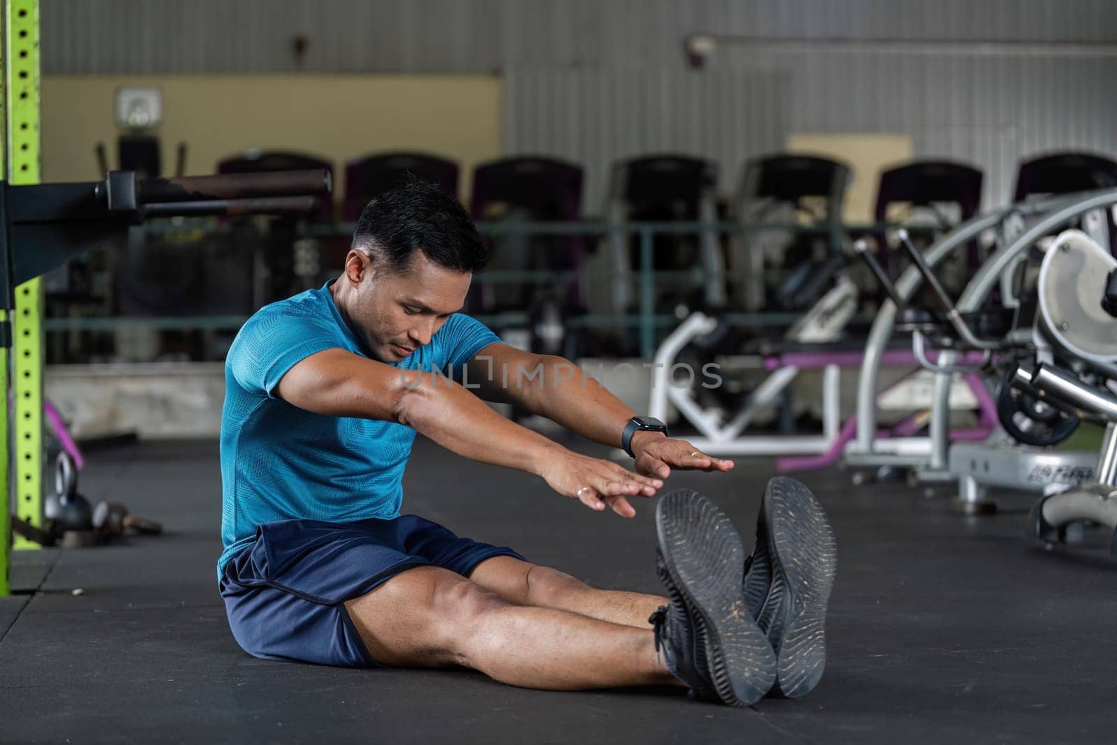 A man performing a stretching exercise on the gym floor, focusing on flexibility and fitness. The atmosphere is energetic and motivating.