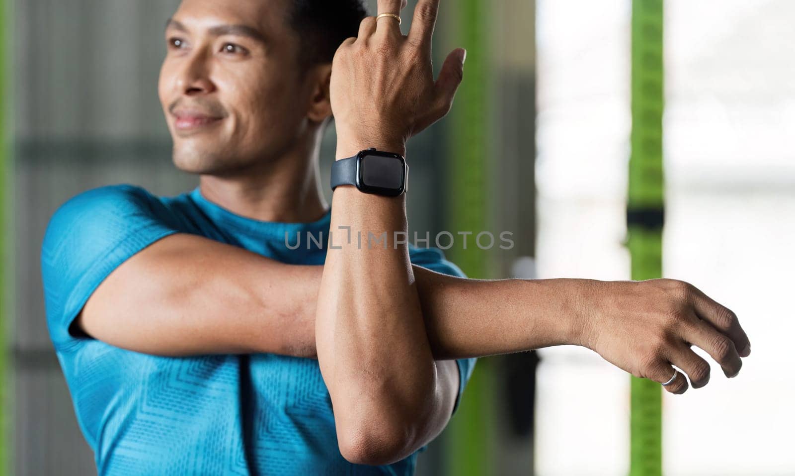 A man performs an arm stretch in a gym, emphasizing the significance of flexibility and warm-up exercises in fitness.
