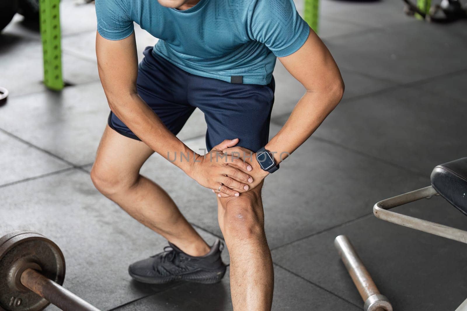A man in a gym setting holds his knee in discomfort, highlighting the importance of injury prevention in fitness routines.