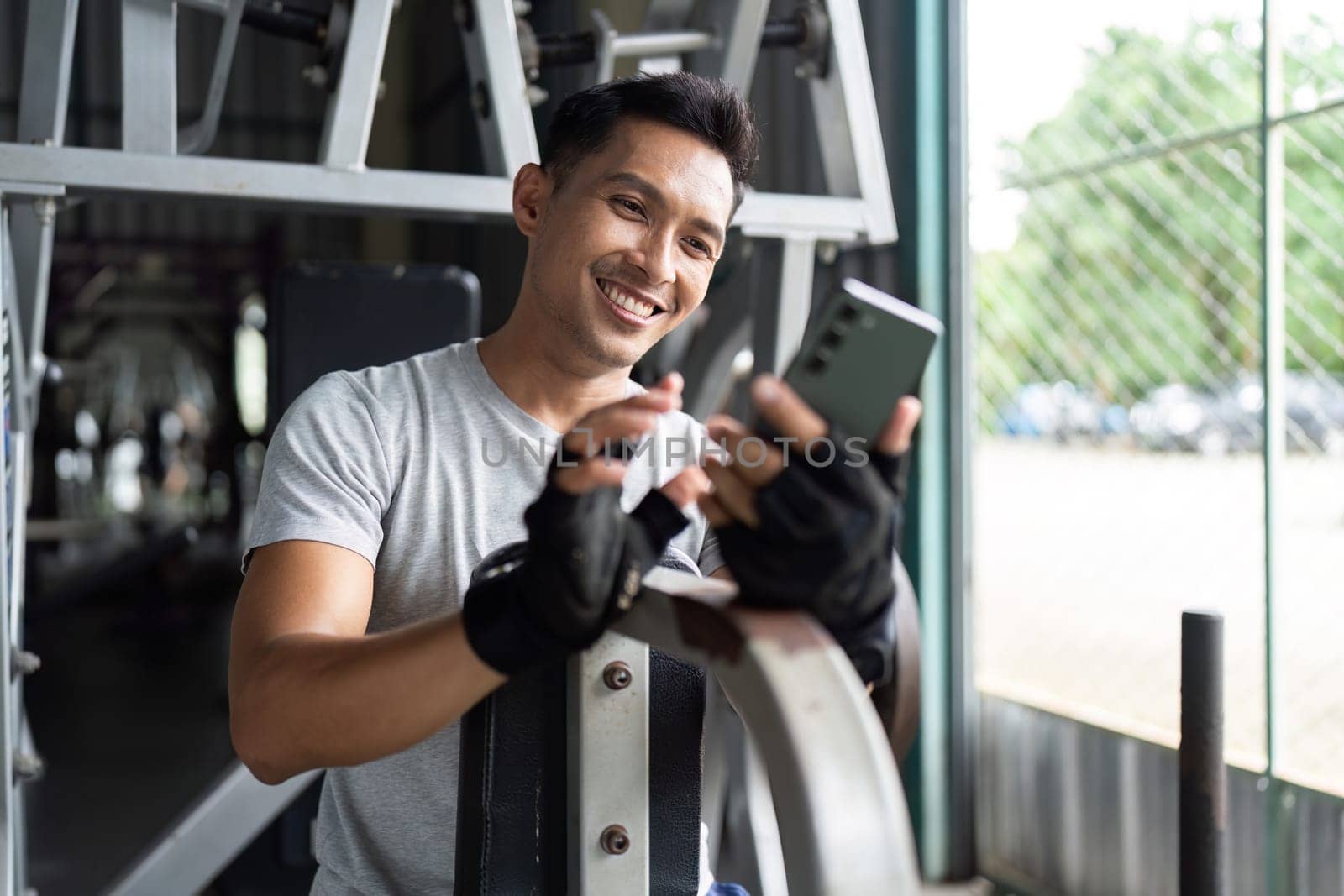 A smiling man checks his smartphone during a break in his workout at the gym, enjoying a moment of relaxation.