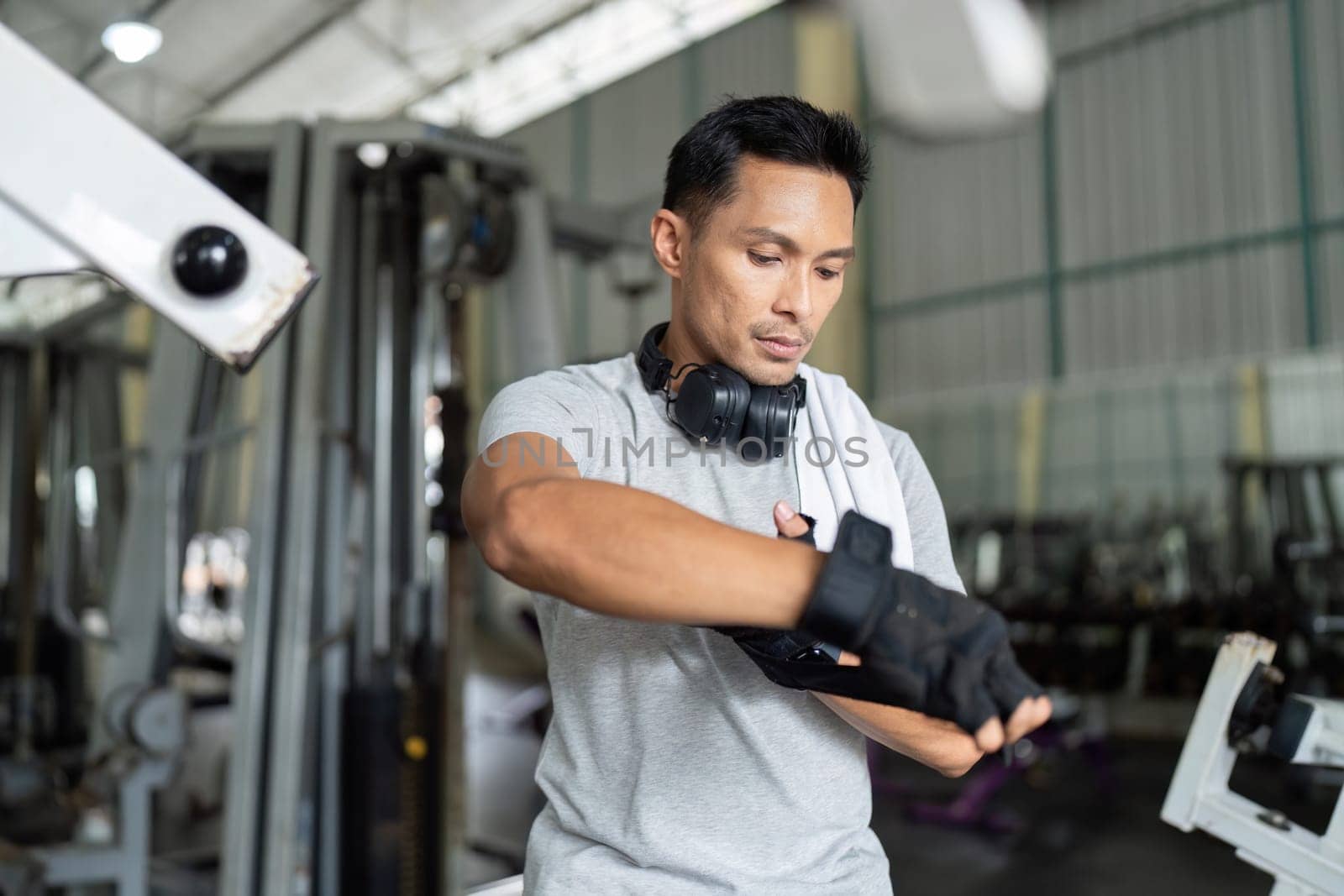 A focused man in a gym setting adjusts his workout gloves and headphones, ready for an intense training session.