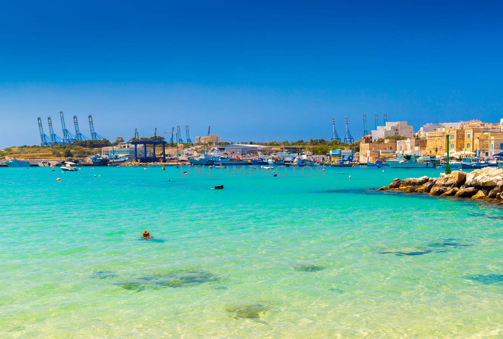 A beautiful view of the small Maltese town of Marsaxlokk with turquoise clear sea water and the port in the background.