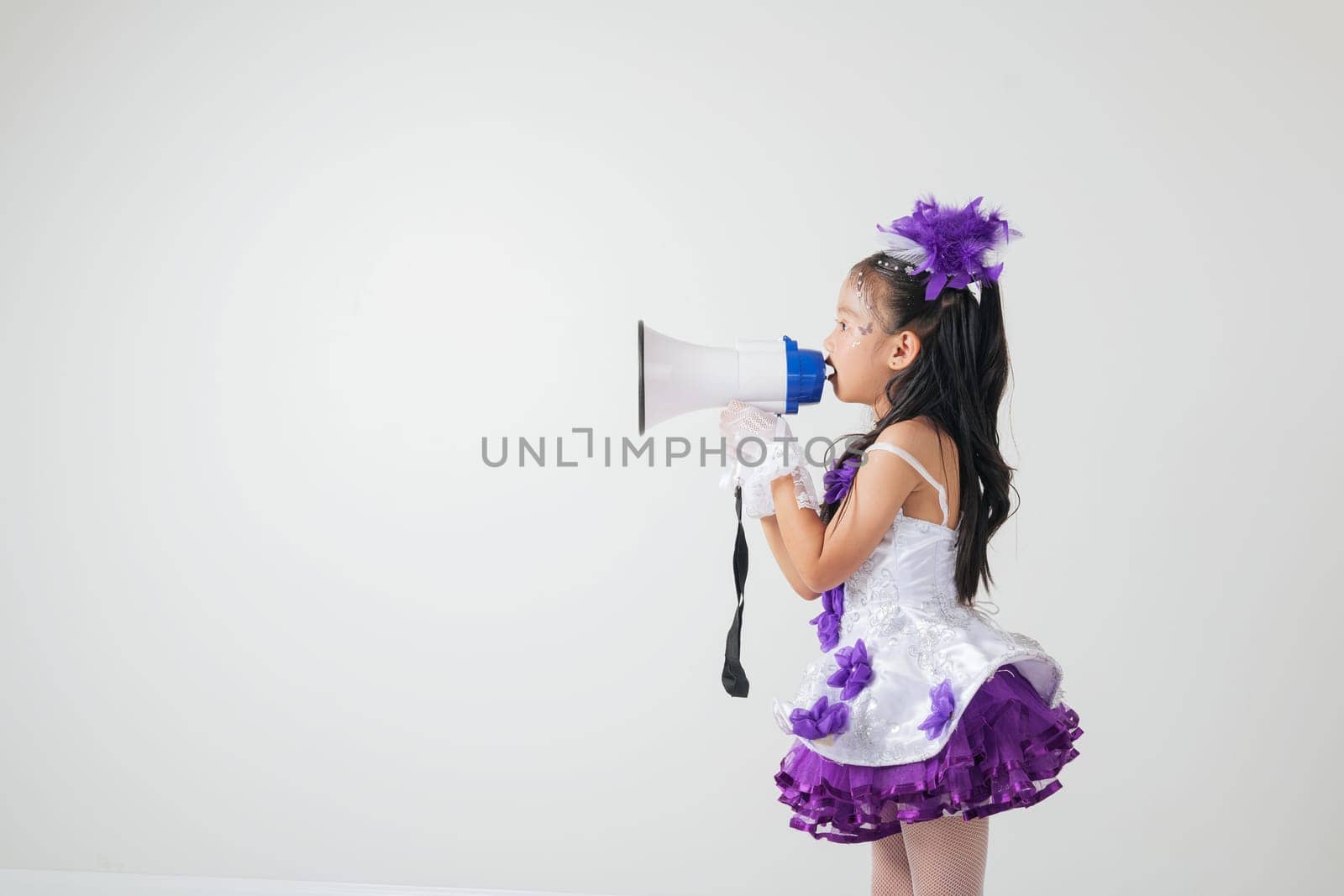 Cheerleader girl in a purple and white outfit using a megaphone. Studio shot on white background, showcasing her energetic, festive, and spirited vibe. A fun portrait of a young cheerleader.