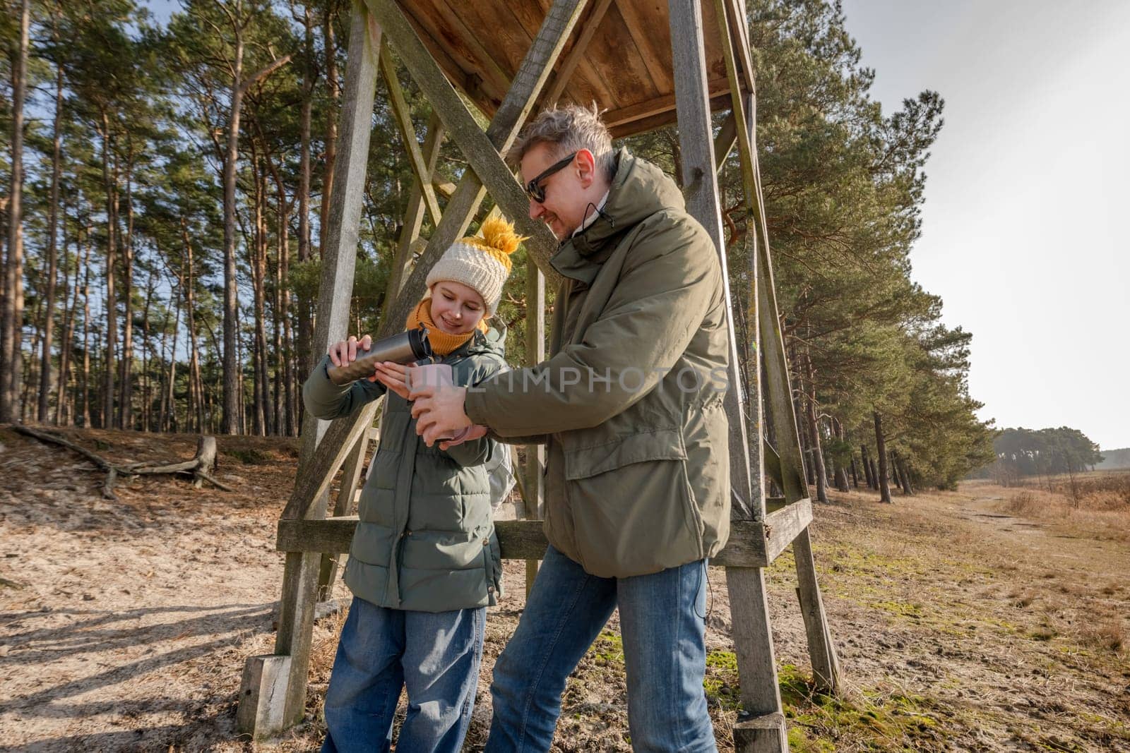 Dad And Daughter Drinking Tea From A Thermos Near The Observation Tower In Spring