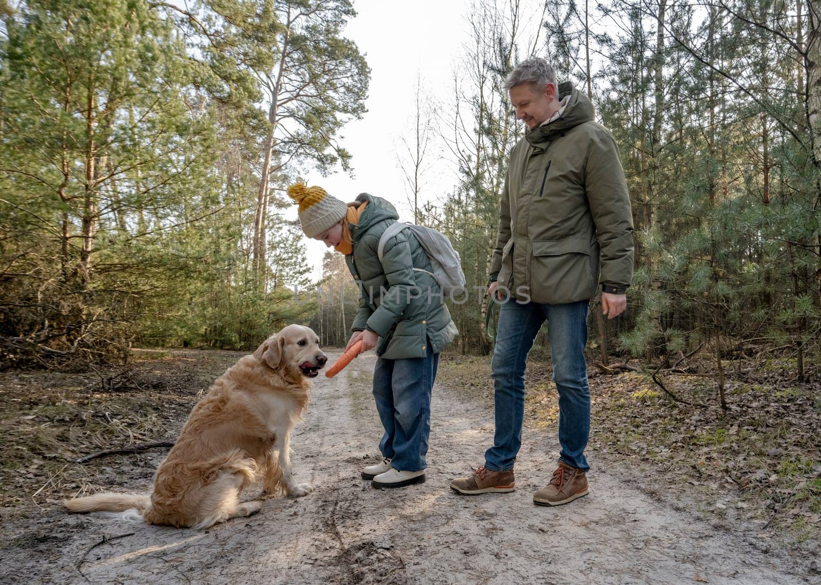 Dad And Daughter Walking In The Forest With A Golden Retriever In Spring
