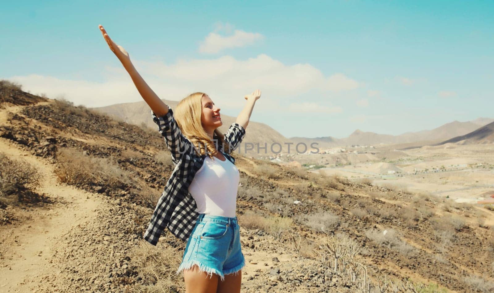 Happy cheerful young woman raising her hands up on hiking trail on top of the mountain, Tenerife, Canary Islands, Spain