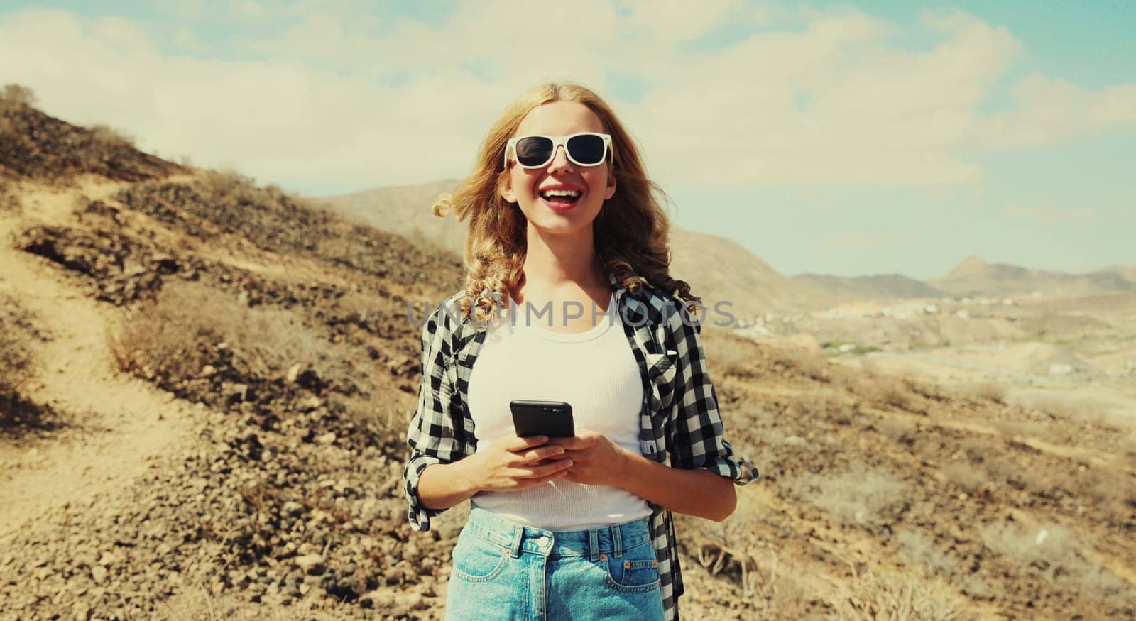 Happy cheerful young woman with mobile phone on a hiking trail on top of the mountain, Tenerife, Canary Islands, Spain