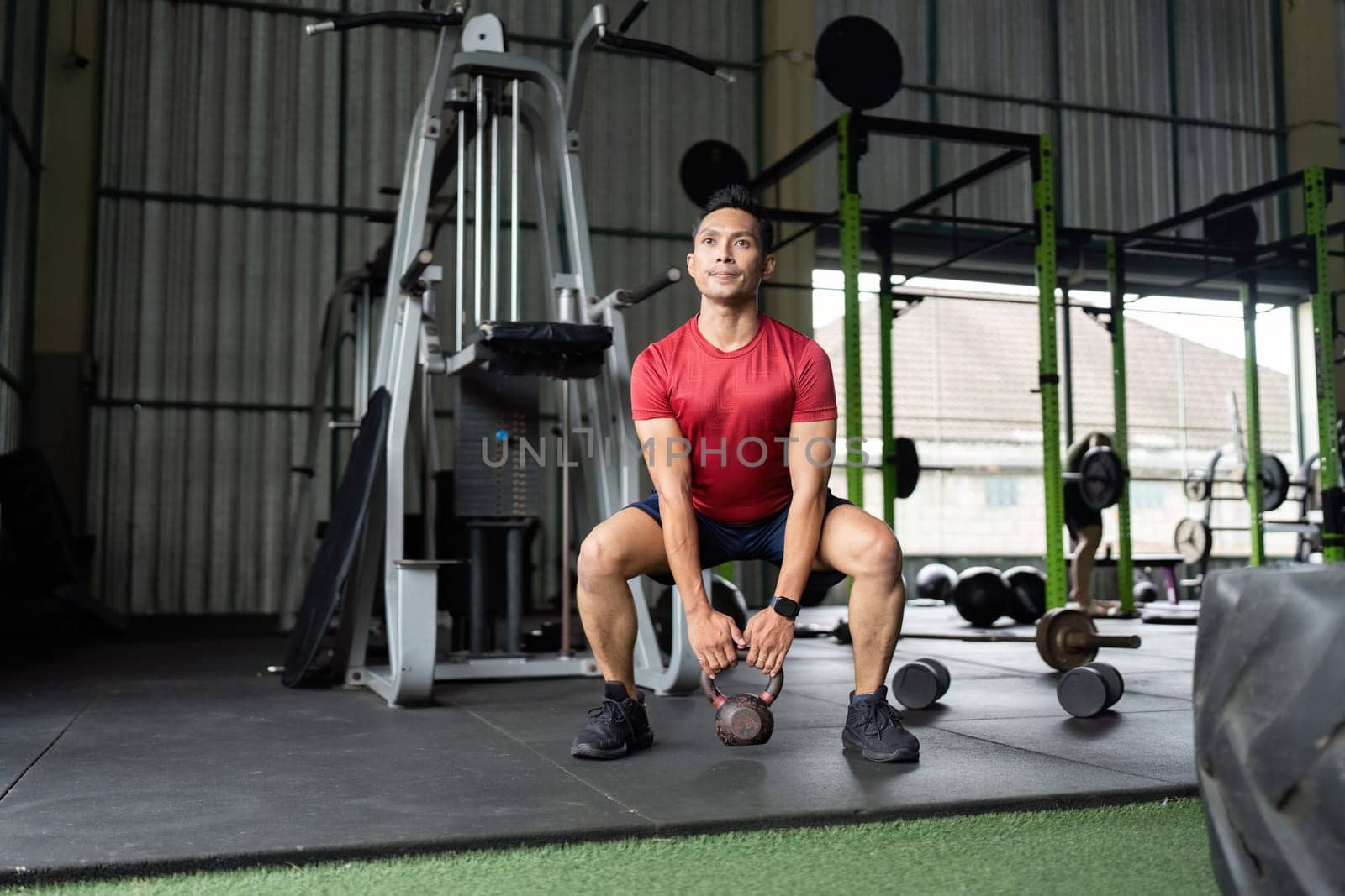 A fit man executes a kettlebell swing, enhancing his full body strength in a gym environment.