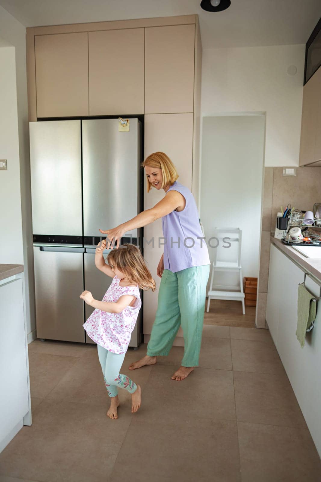 A mother and daughter share laughter while dancing together.