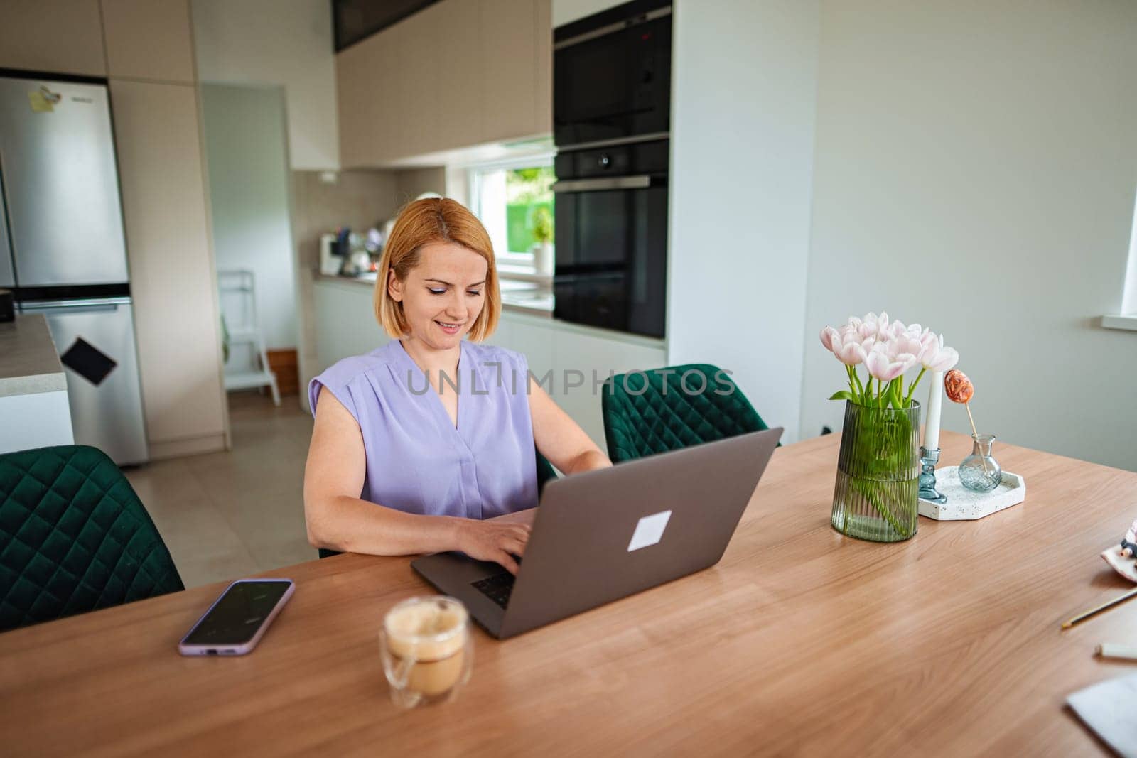 A woman happily types on her laptop with a drink.