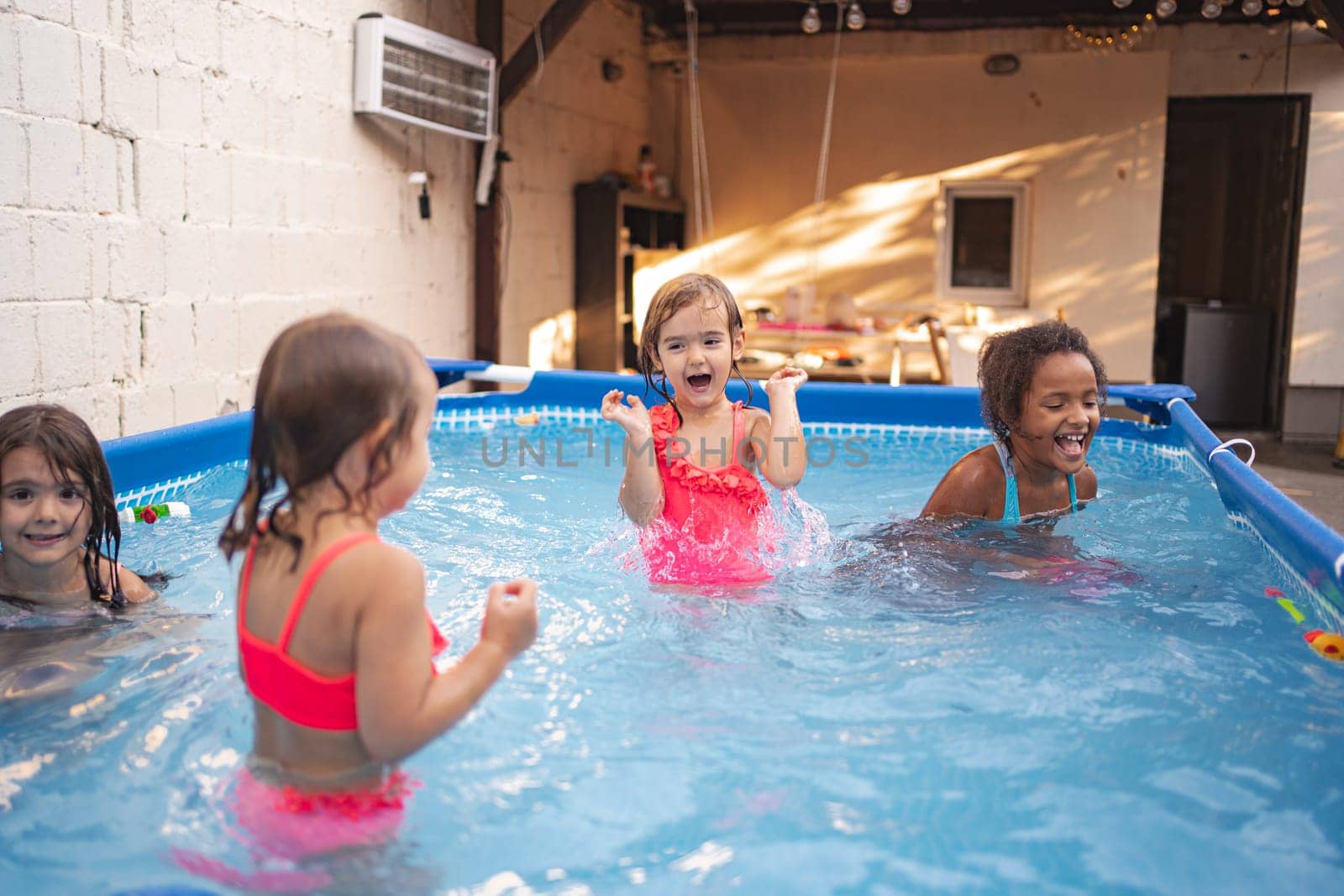 Four kids splash and play joyfully in an inflatable pool outdoors.