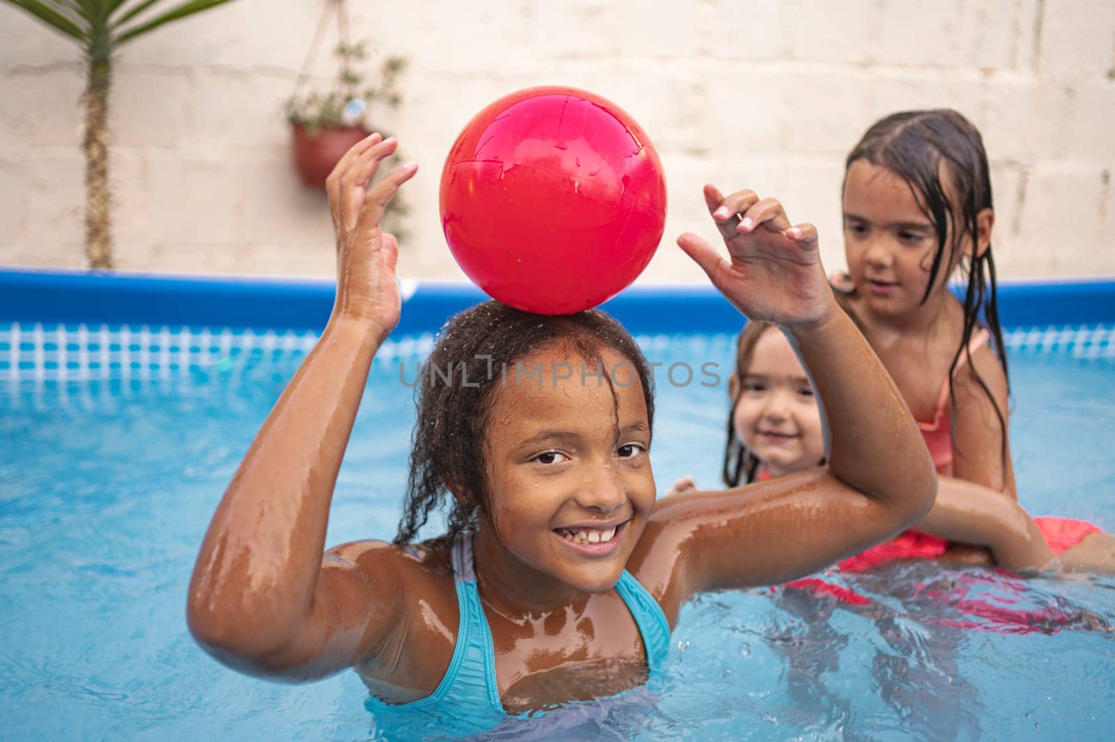 Three children have fun playing with a red ball in a pool.