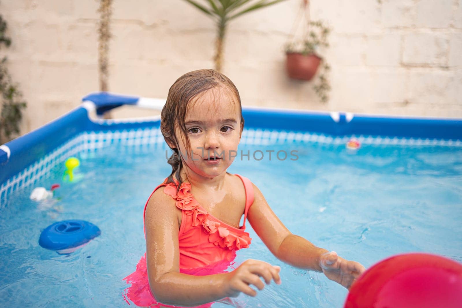 A girl splashes in a swimming pool filled with toys on a sunny day.