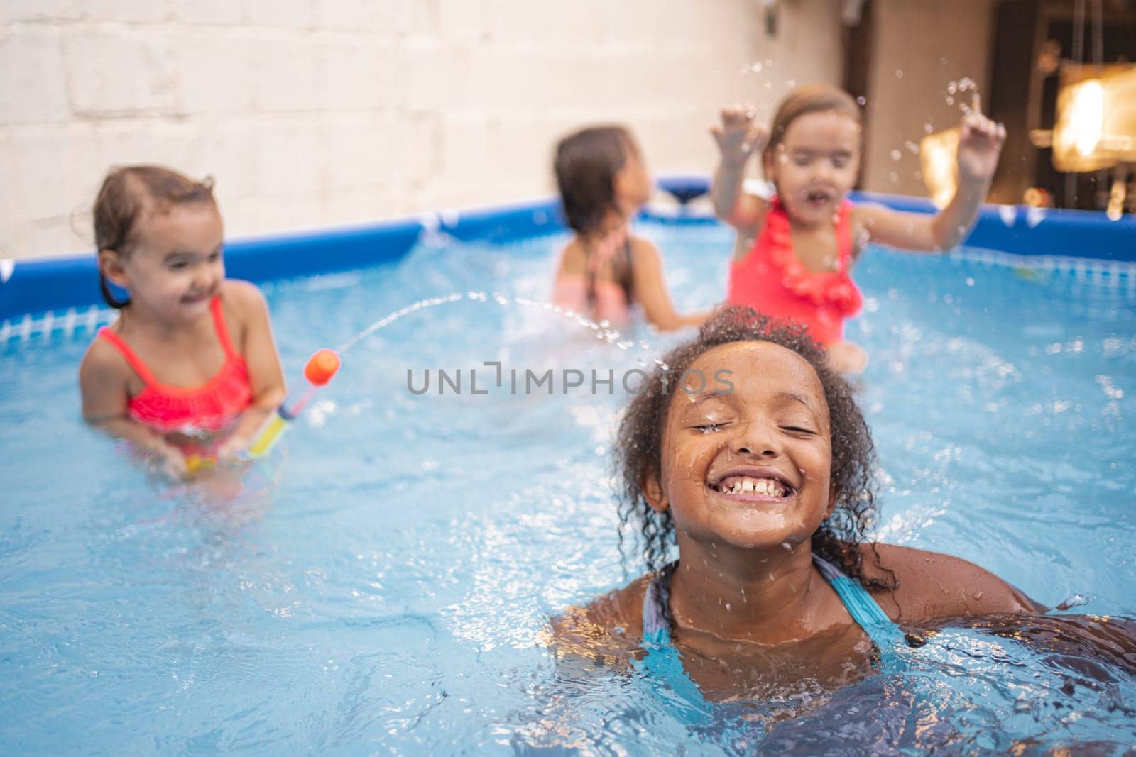 Four kids splash around in a backyard pool under bright sunshine.