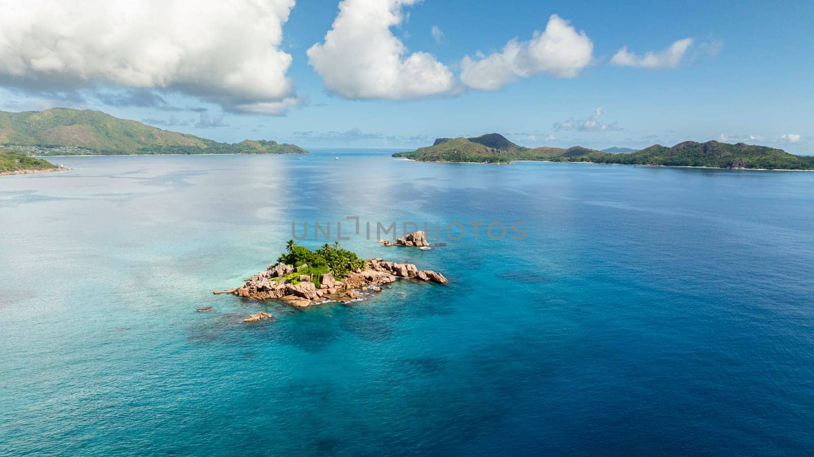 A small, rocky island covered in greenery sits in the middle of expansive turquoise waters. St Pierre, Curieuse Islands. Seychelles.