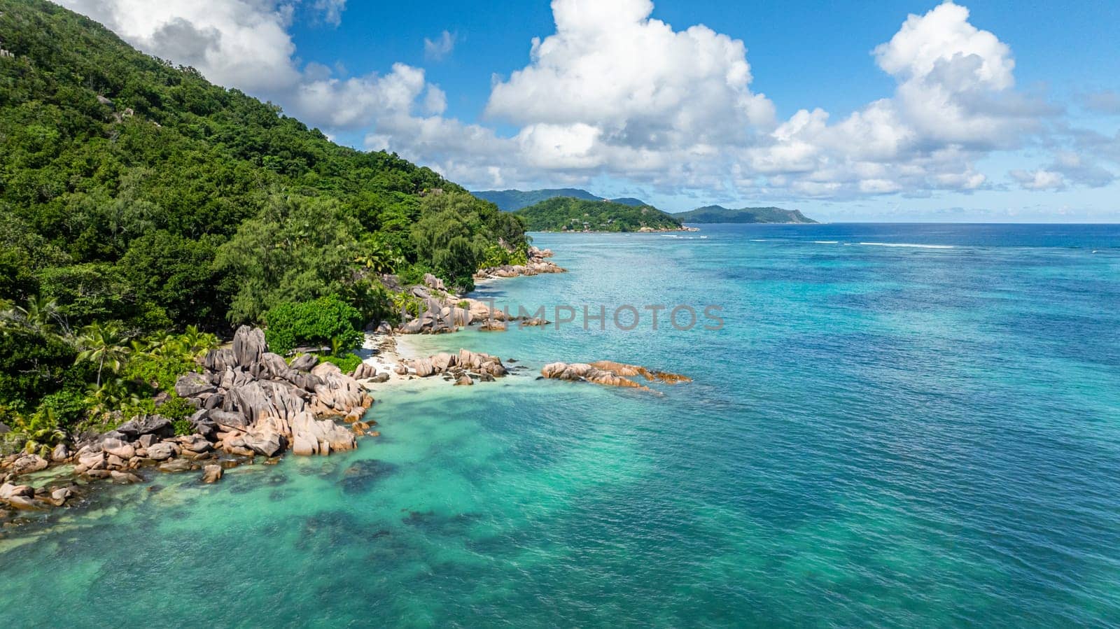 A scenic tropical coastline featuring large rocks, lush green vegetation, and beach. Praslin, Seychelles.