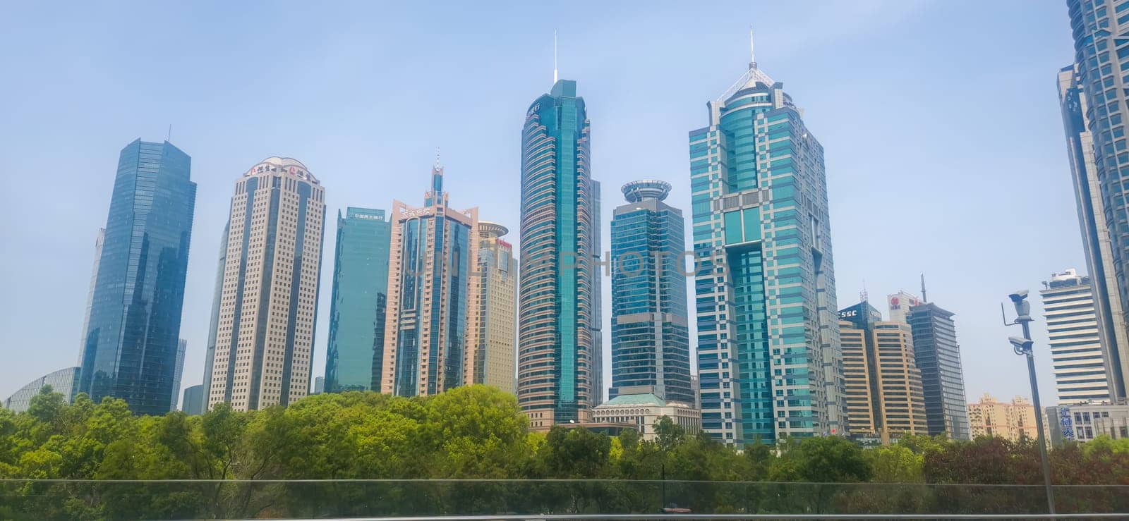 Shanghai, China - 1 April 2025: Modern skyline of Lujiazui, Pudong with tall skyscrapers above green trees under a clear blue spring sky