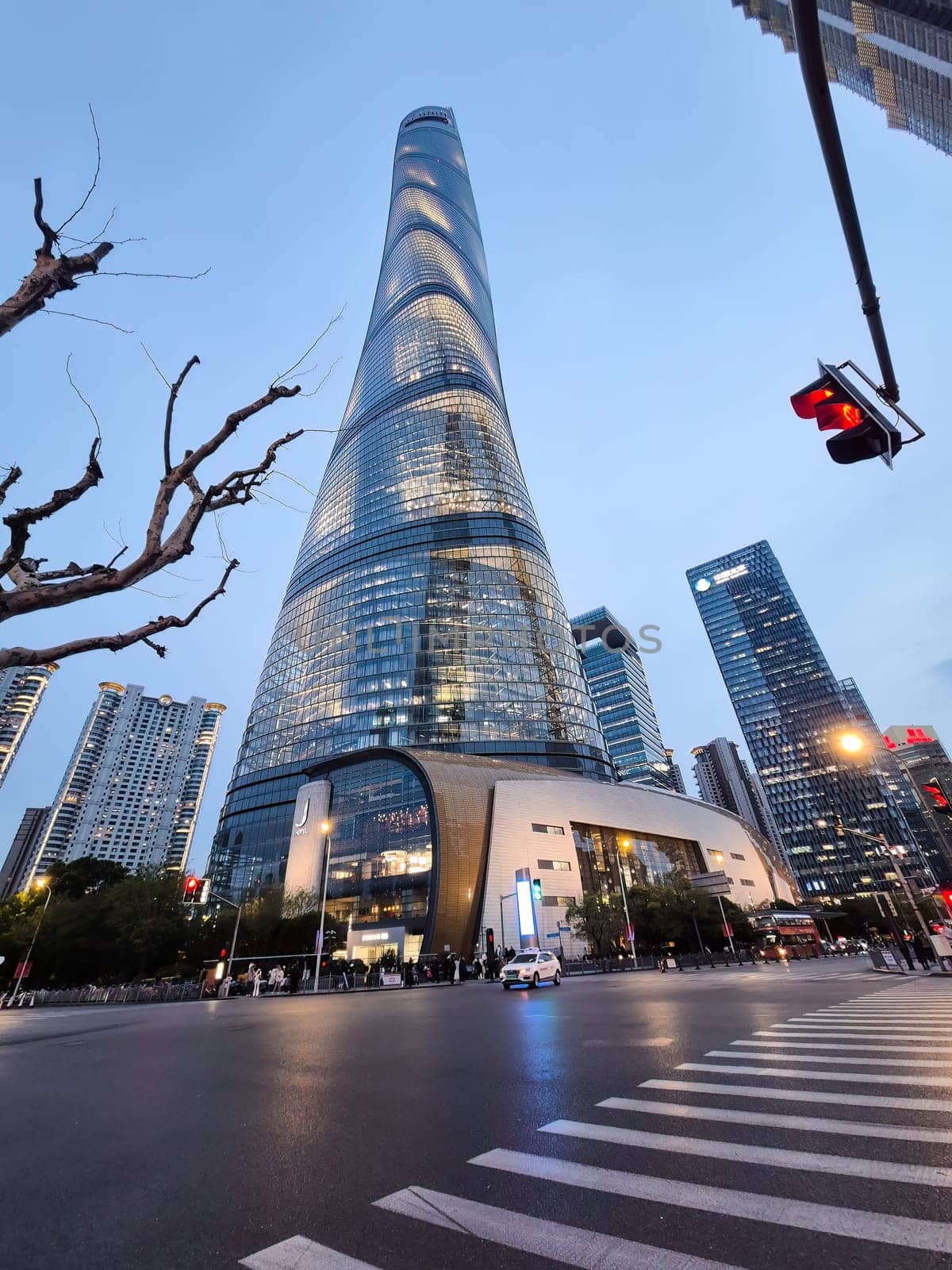 Shanghai, China - 1 April 2025: View of the Shanghai Tower at dusk, surrounded by modern skyscrapers and city life at a busy downtown intersection.