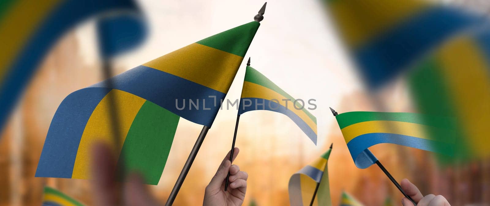 Gabon flags in their hands on a blurred urban background. The photo illustration was created without the use of artificial intelligence, only using Photoshop.